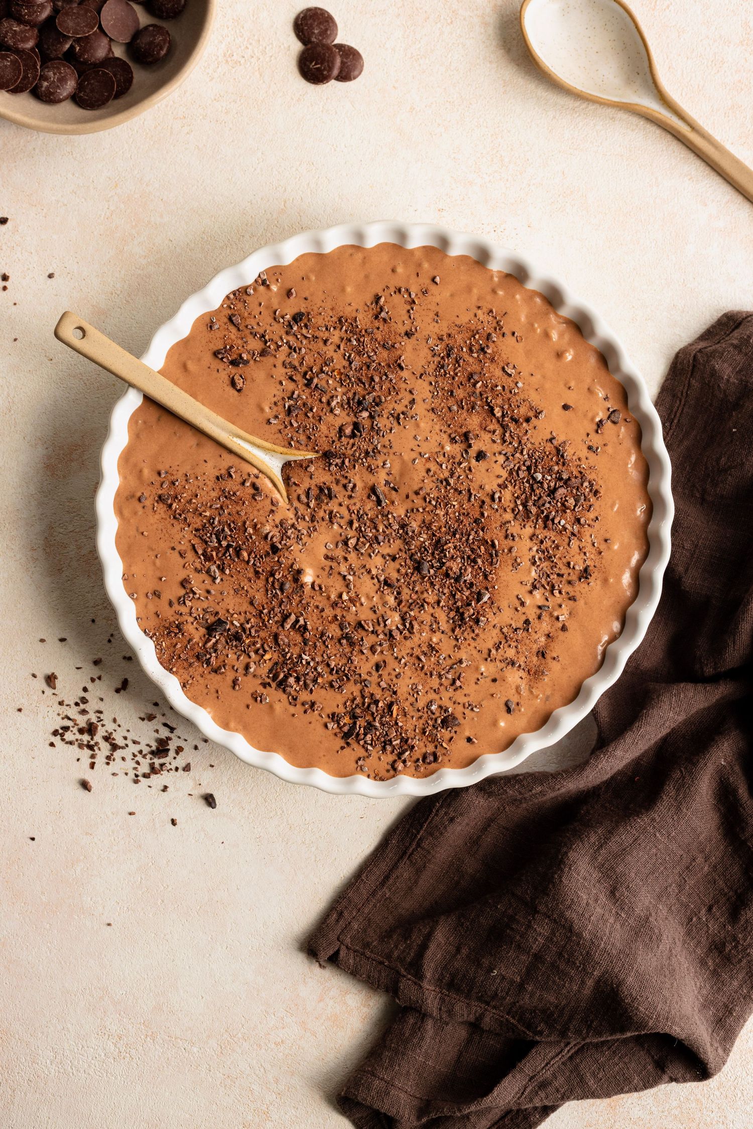 Chocolate mousse tart in white fluted dish topped with cocoa powder and chocolate shavings, gold spoon resting on top.