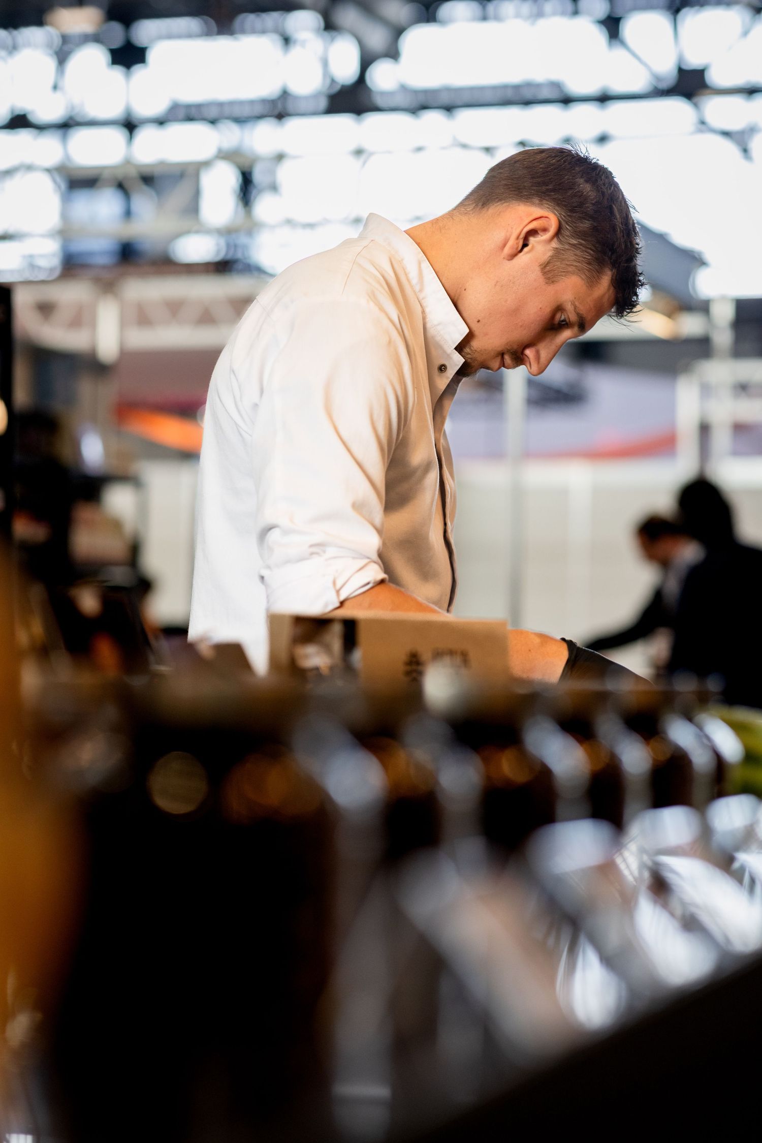 Man in white shirt examining wine bottles at a trade show exhibition event.