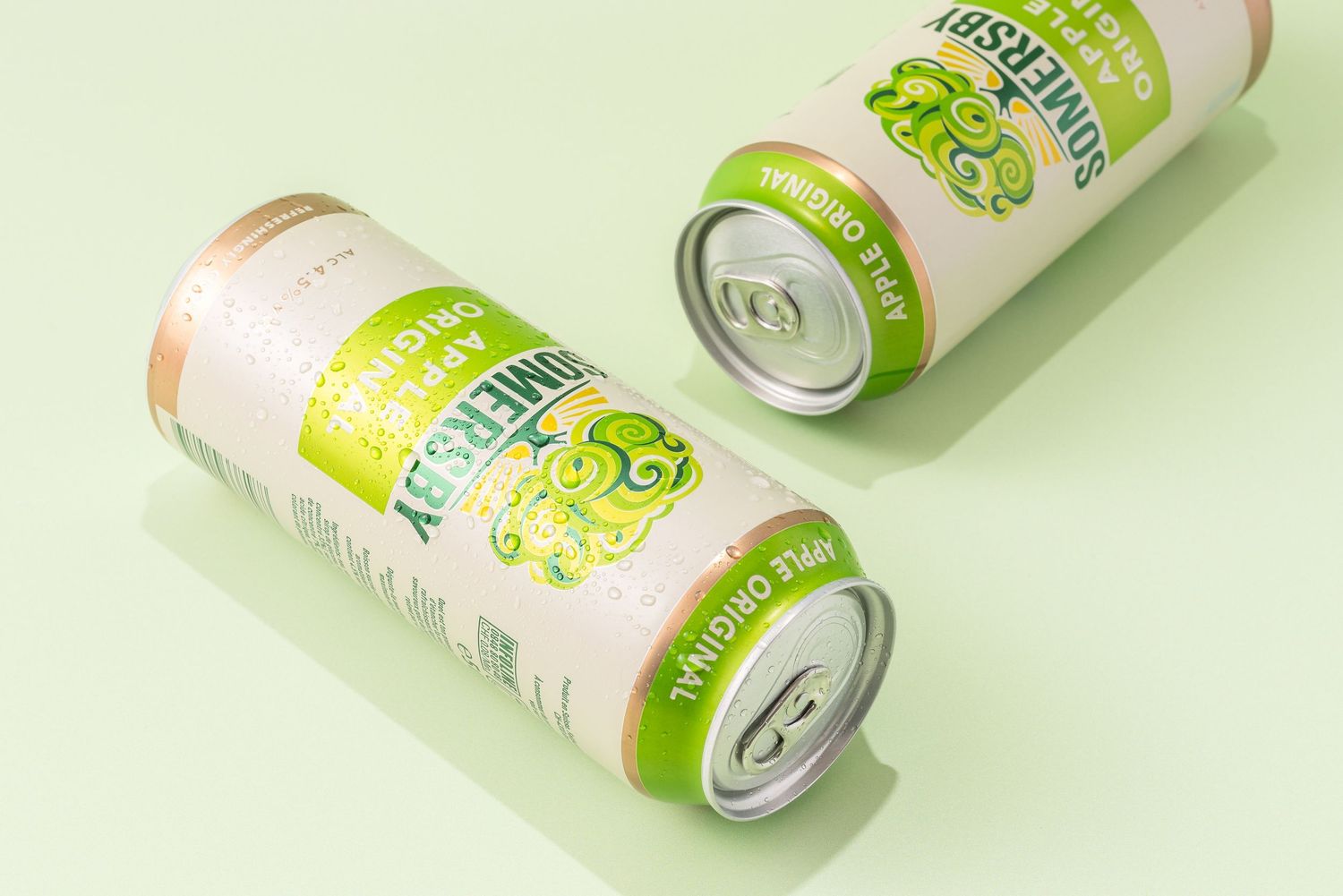 Three white and green beverage cans with fresh citrus design lying on white surface.