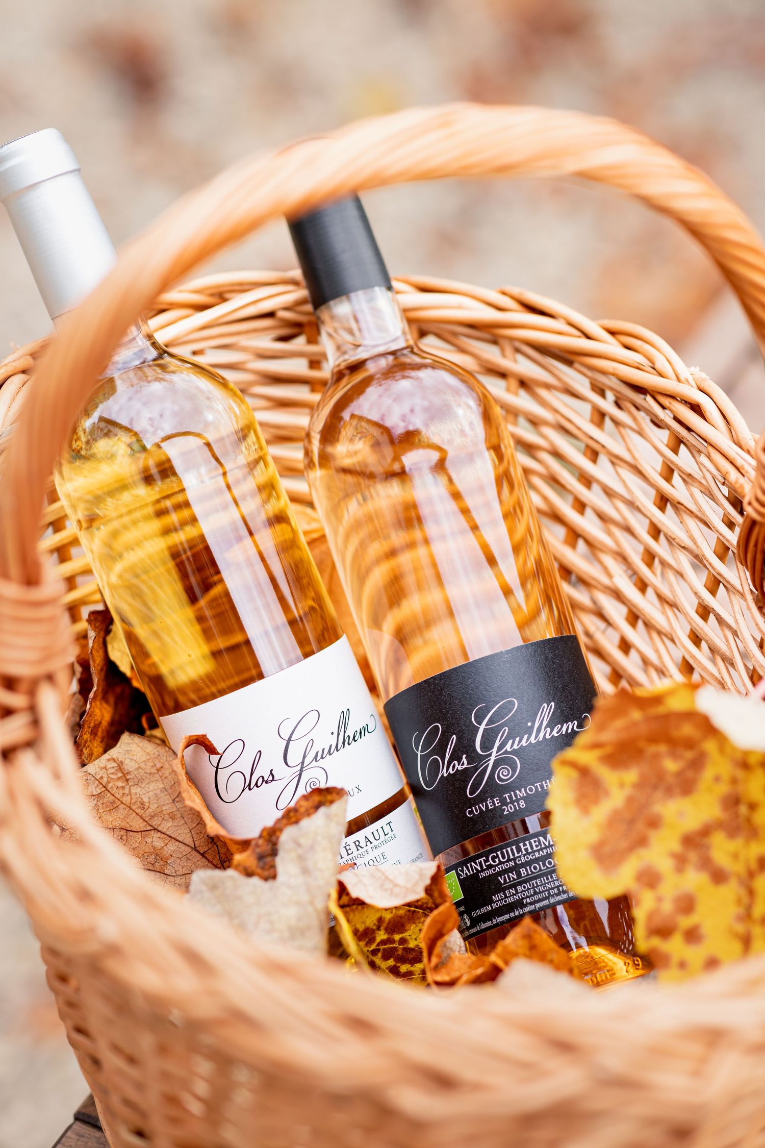 Two Clos Guilhem wine bottles nestled in a wicker basket with autumn leaves, showcasing rosé wines from Saint-Guilhem.
