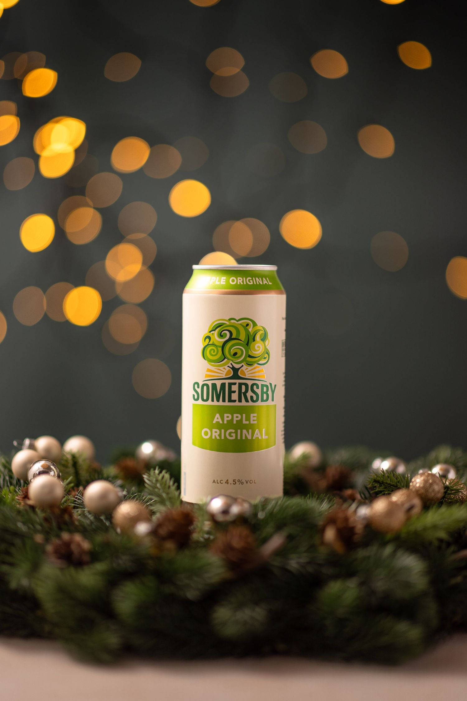 A can of Somersby apple cider sits on a festive evergreen garland with silver ornaments and bokeh lights in the background.