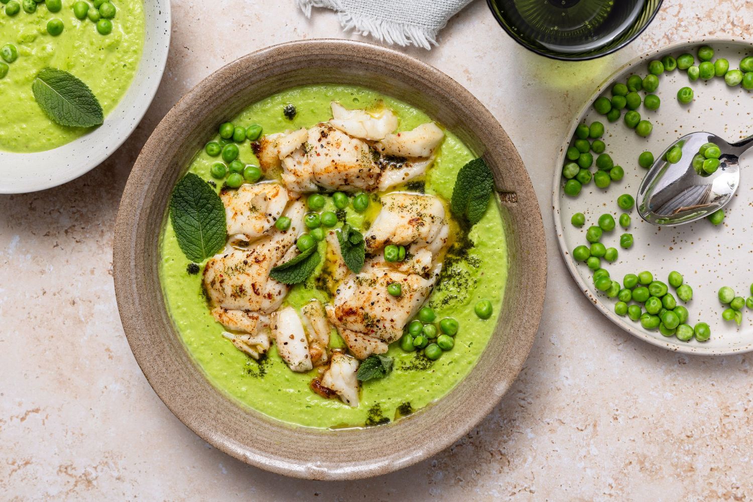 Grilled fish served on vibrant green pea puree with fresh mint leaves in a ceramic bowl, garnished with whole peas.