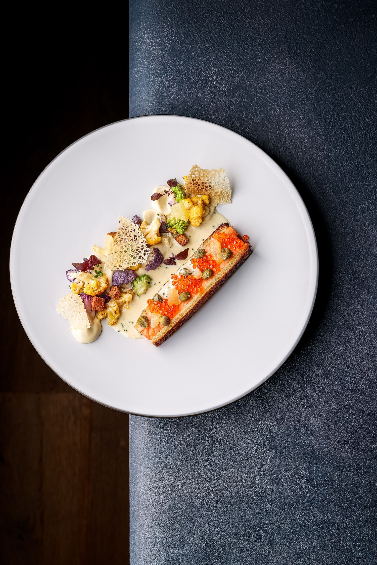 Elegantly plated seafood dish with colorful garnishes served on a white oval plate against a dark background.