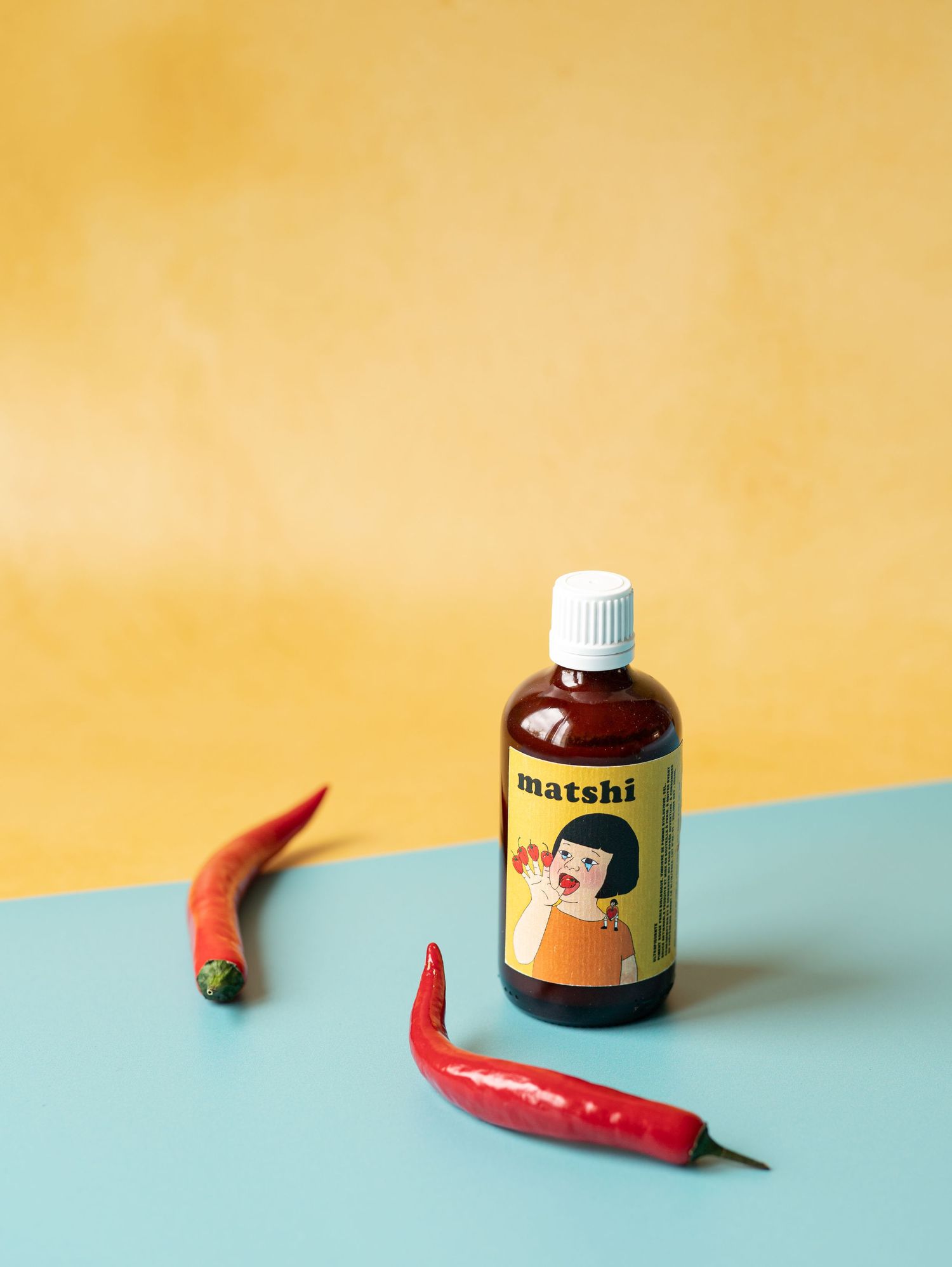 Matshi hot sauce bottle with red chili peppers on a blue and yellow background.