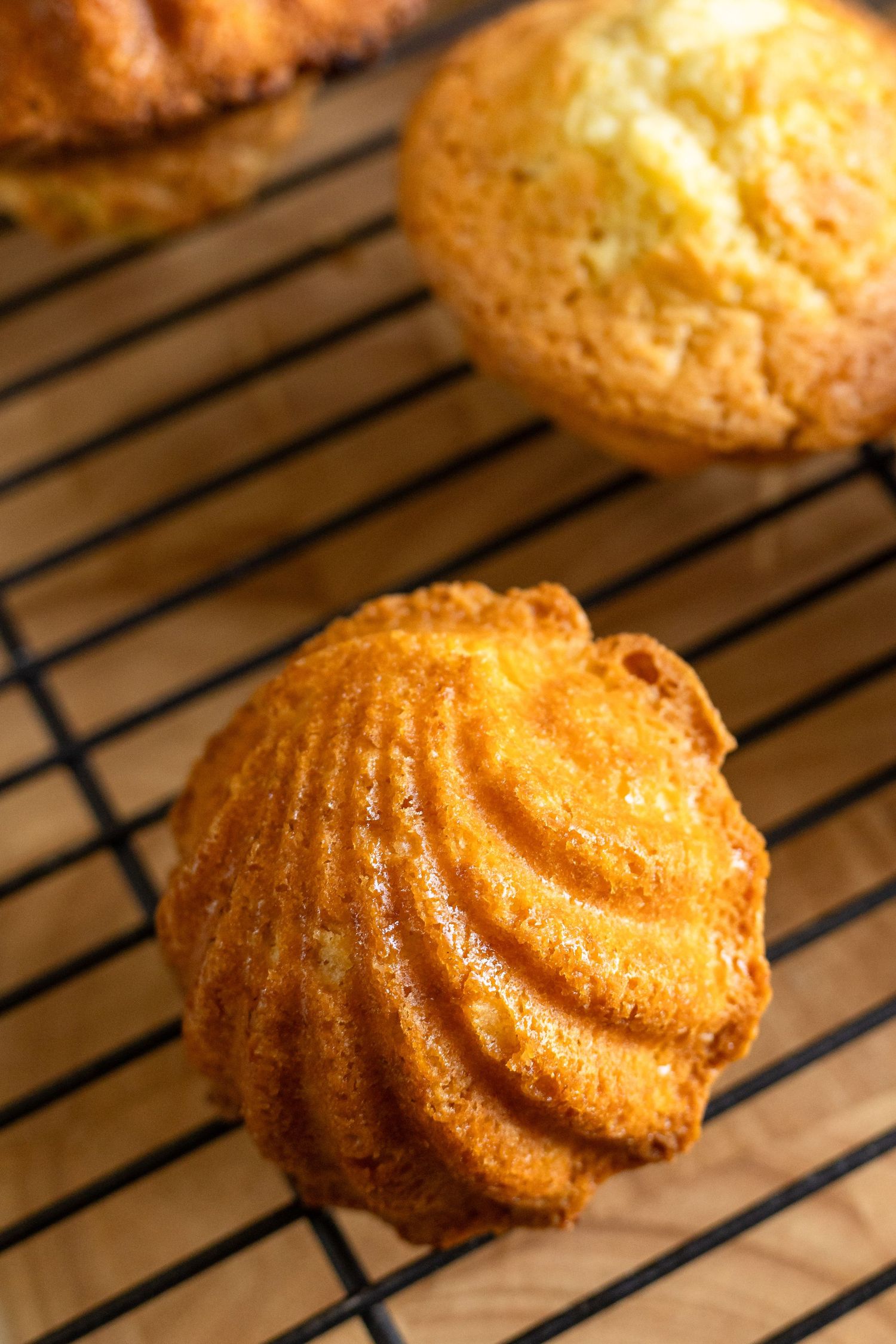 Freshly baked golden muffins cooling on a wire rack, with a ridged bundt-style cake in the foreground.