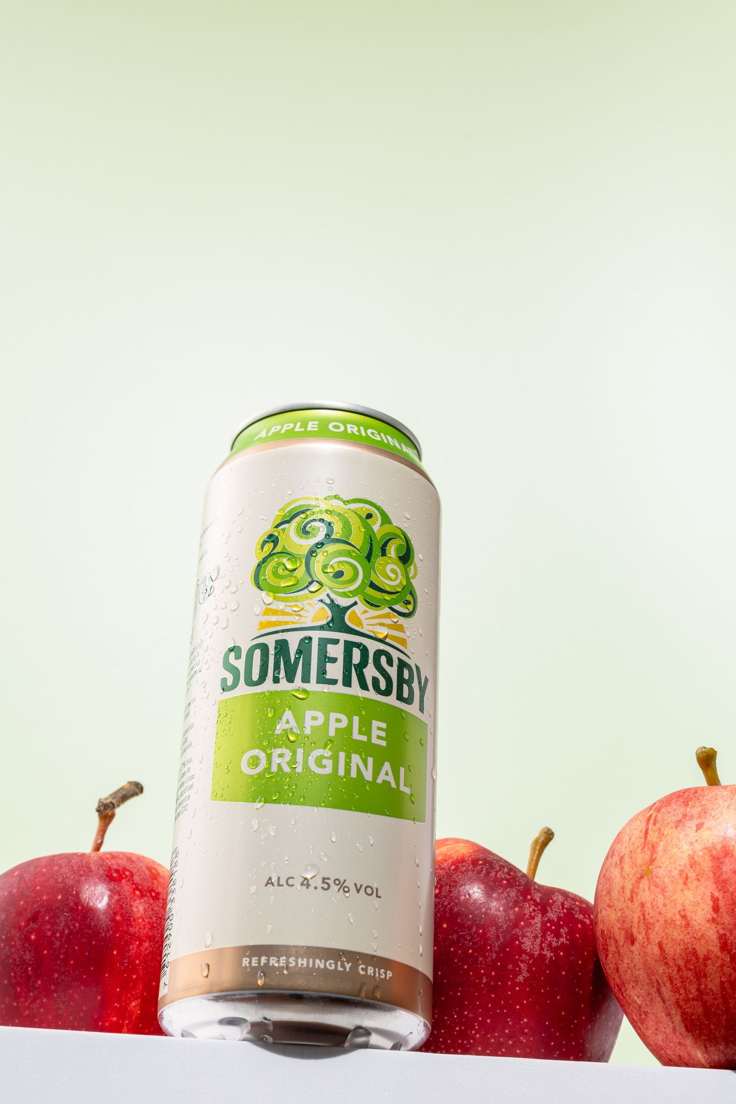 A can of Somersby Apple Original cider positioned with fresh red apples against a light green background.