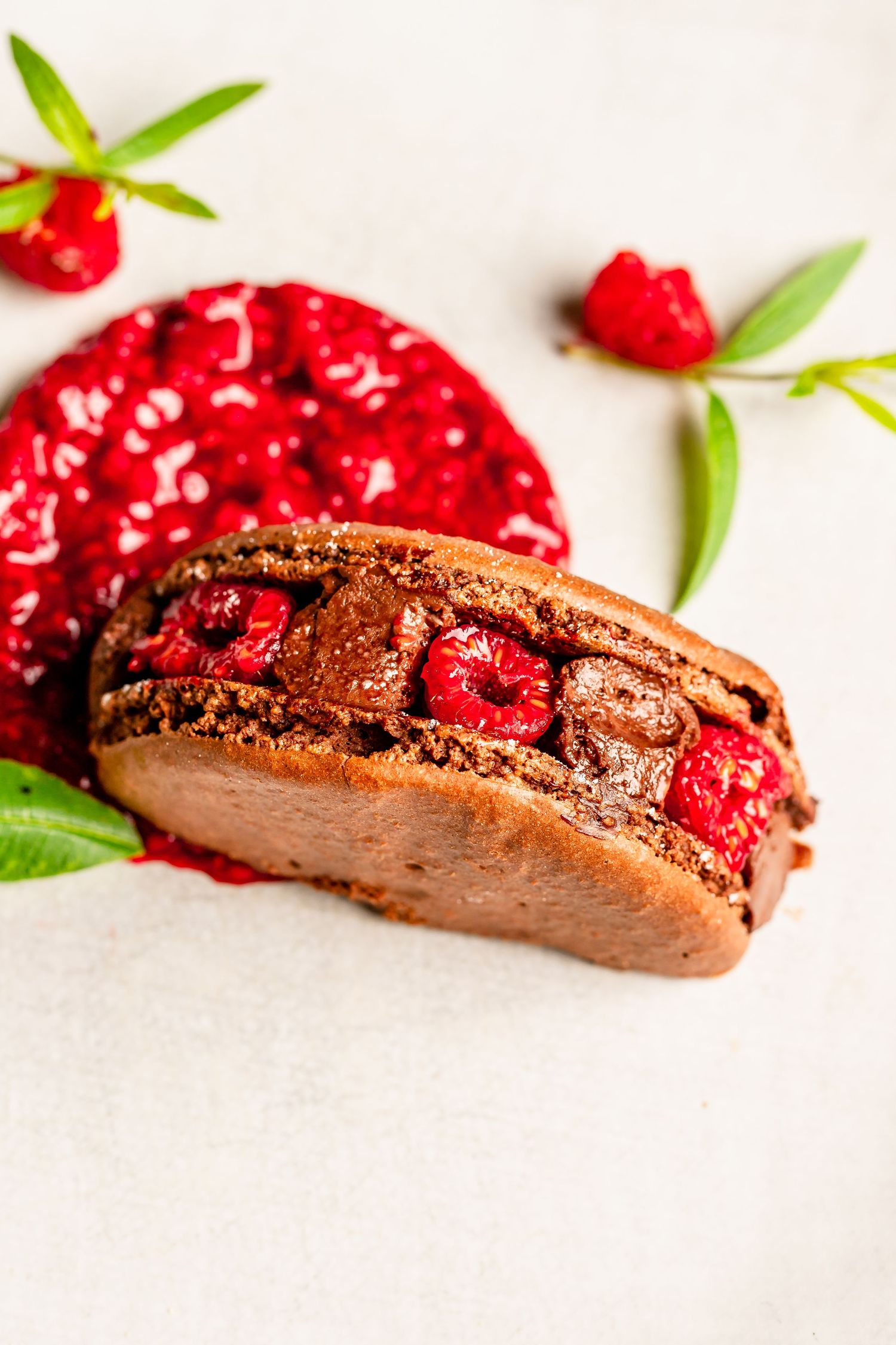 Chocolate macaron filled with raspberries and ganache, served with berry compote and fresh mint leaves.