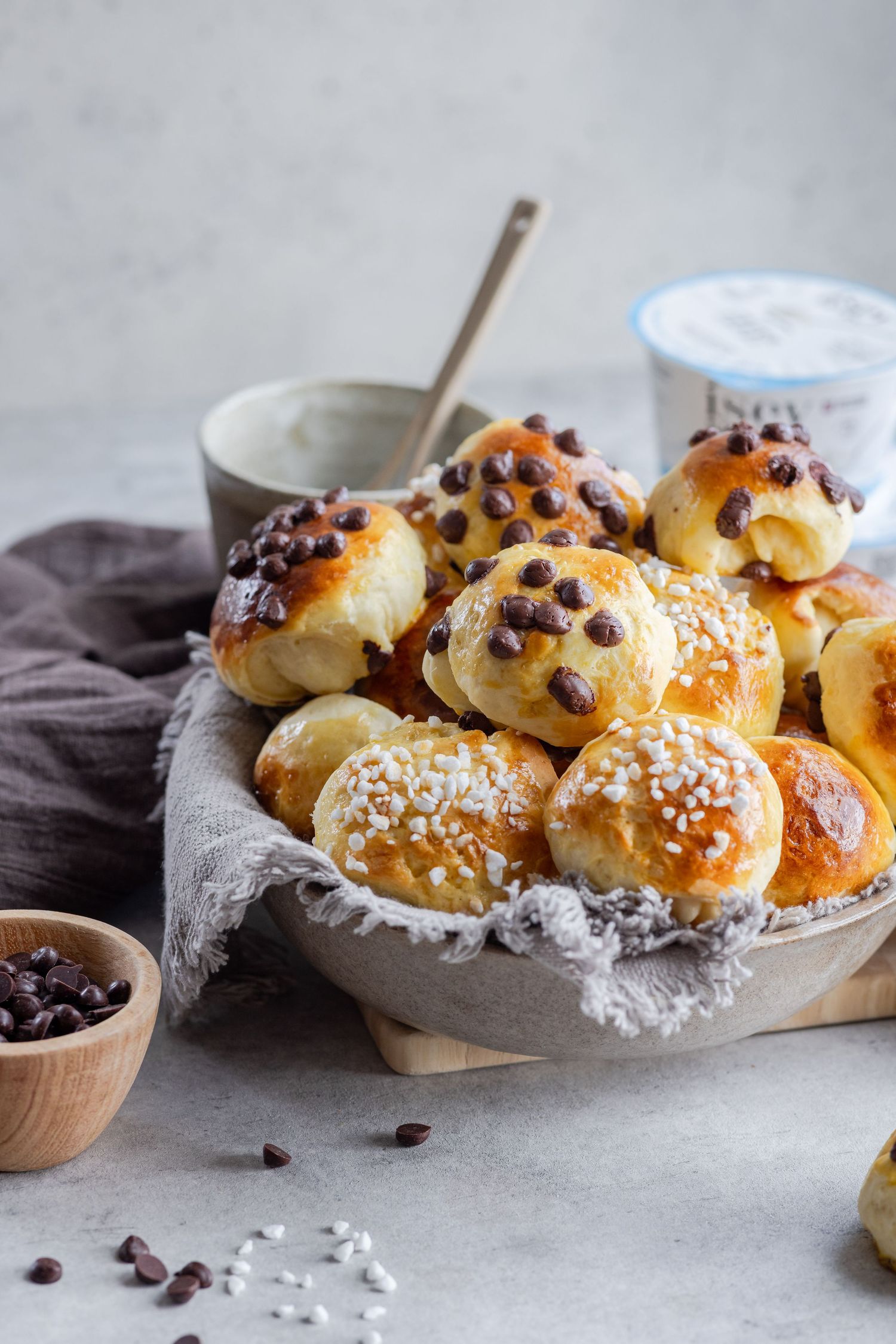 Freshly baked brioche rolls with chocolate chips and pearl sugar in a rustic bowl, served with dipping sauce.