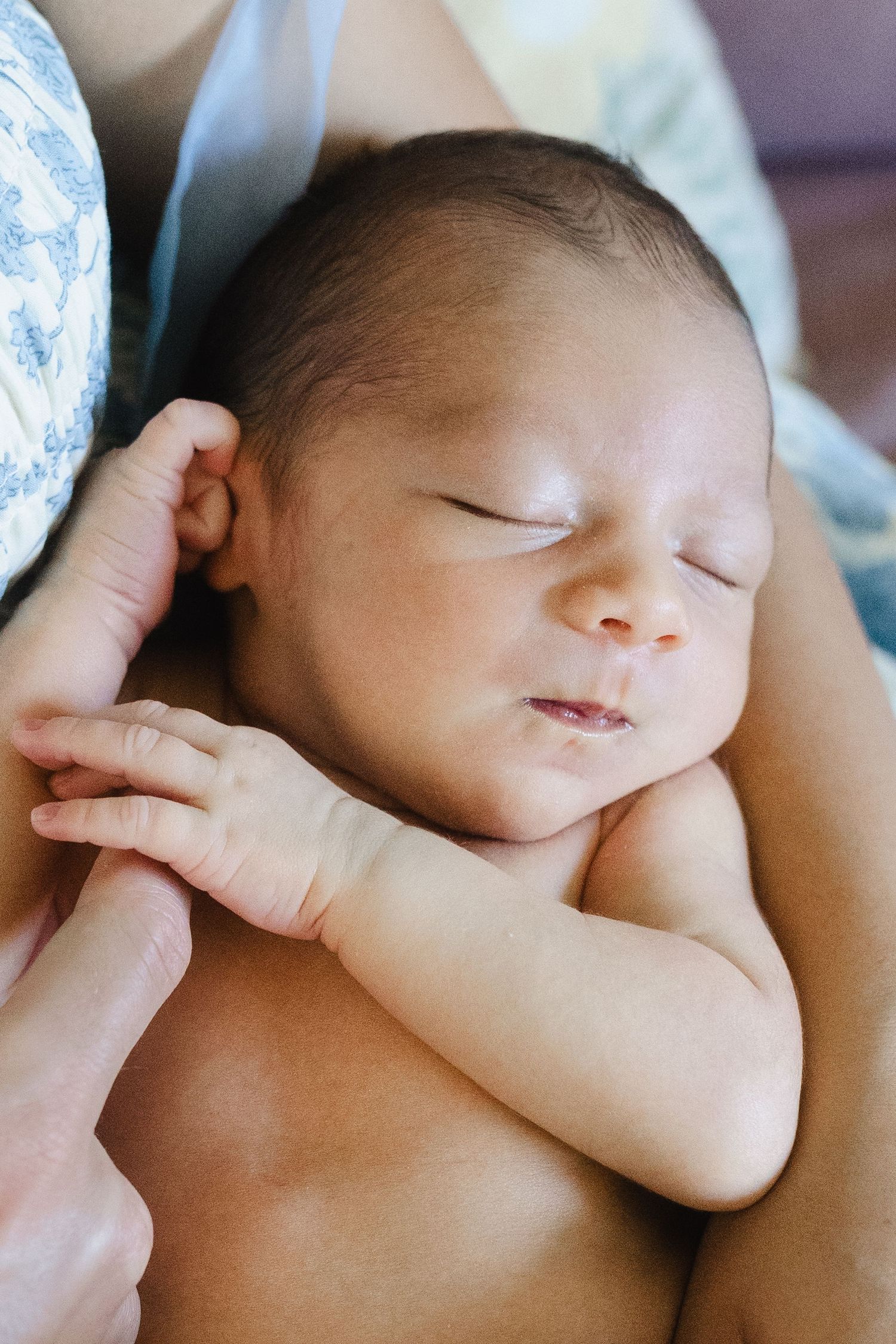 A peaceful sleeping newborn baby with closed eyes and tiny crossed arms rests against a soft background.