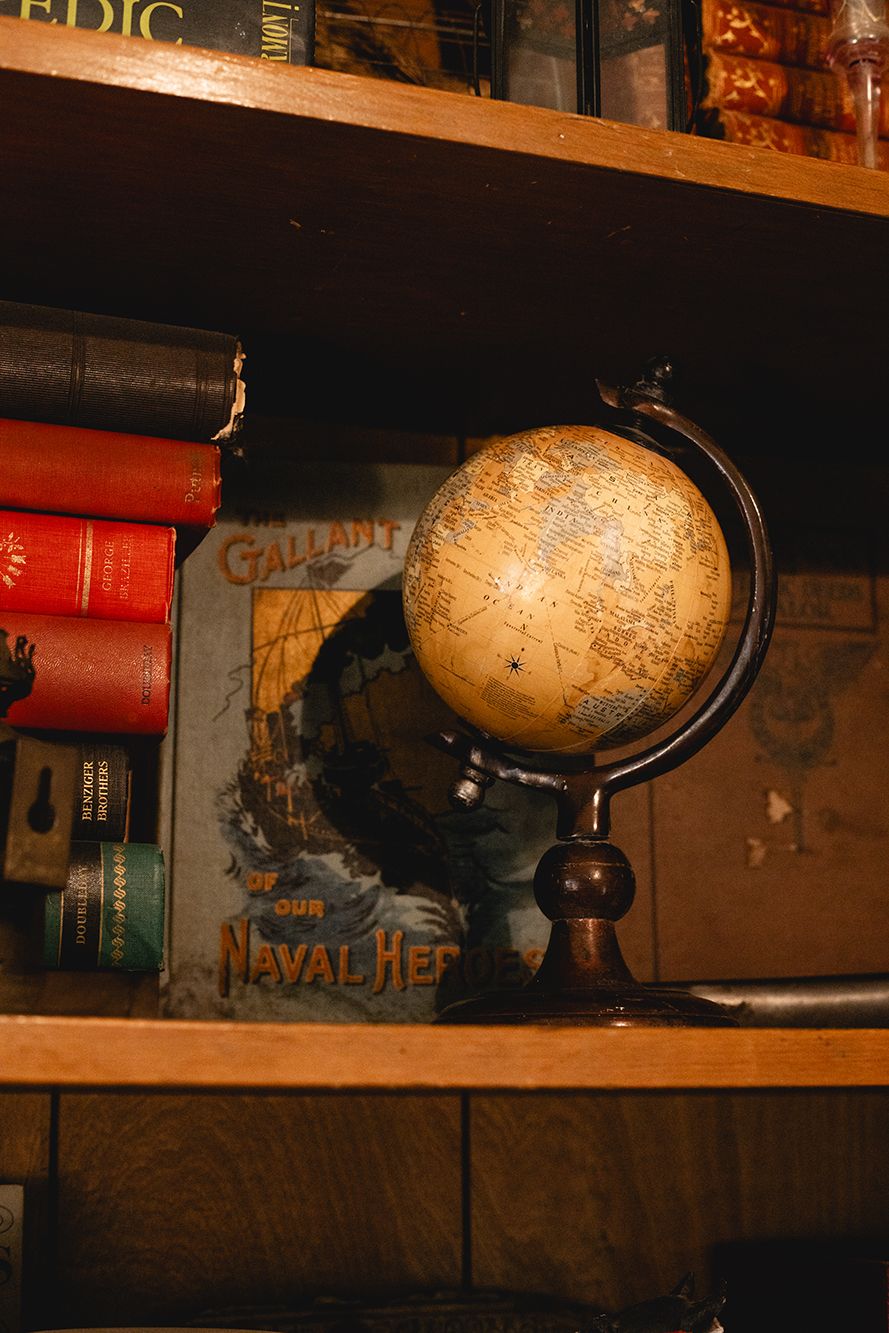 Antique globe and books arranged on wooden shelves in warm lighting.