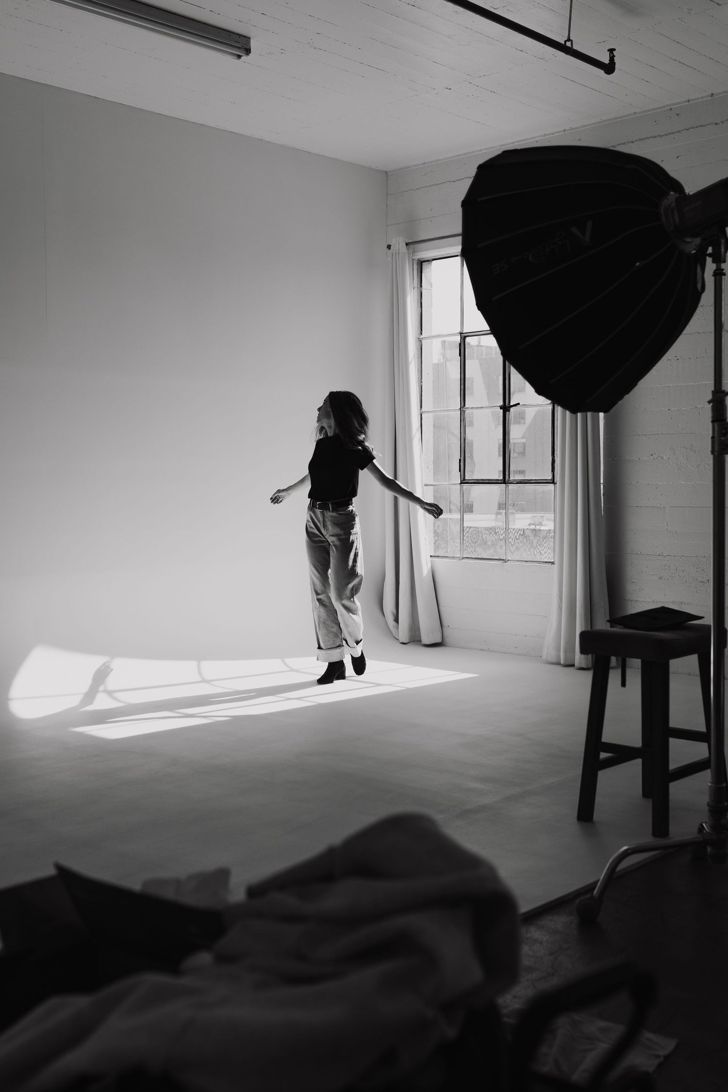 Black and white photo of a person jumping in a studio space with a large softbox light visible in the frame.