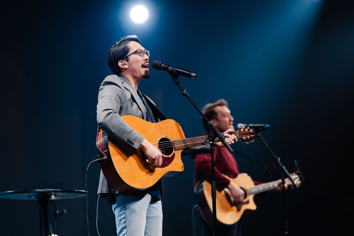 Musicians playing acoustic guitars on stage with dramatic blue backlighting and concert atmosphere.