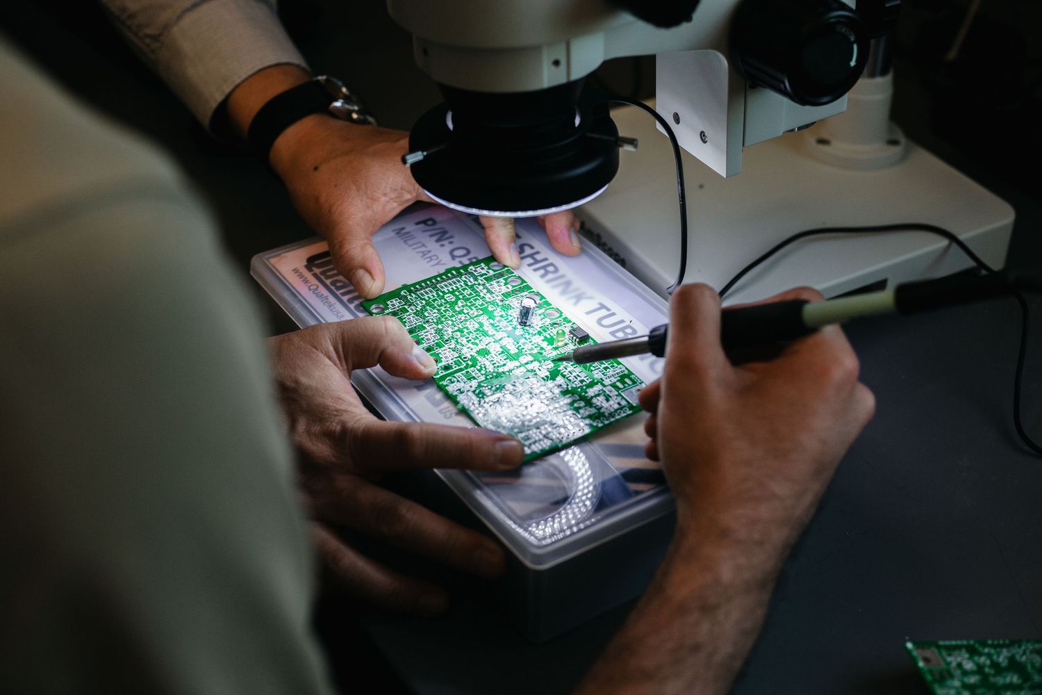 Close-up of hands repairing electronic circuit board with soldering iron and tools.