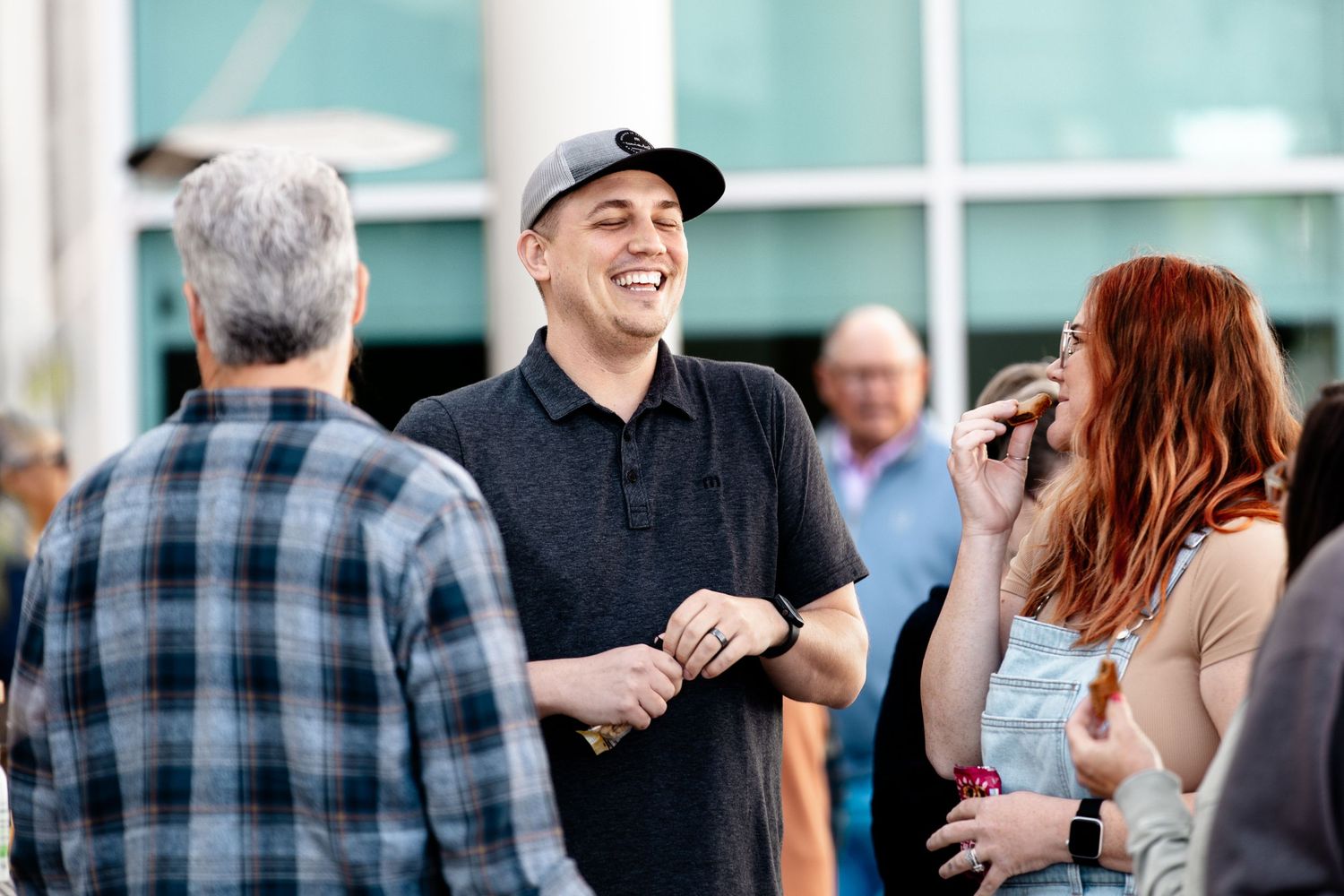 Group of people having casual conversations in an outdoor setting near glass windows.
