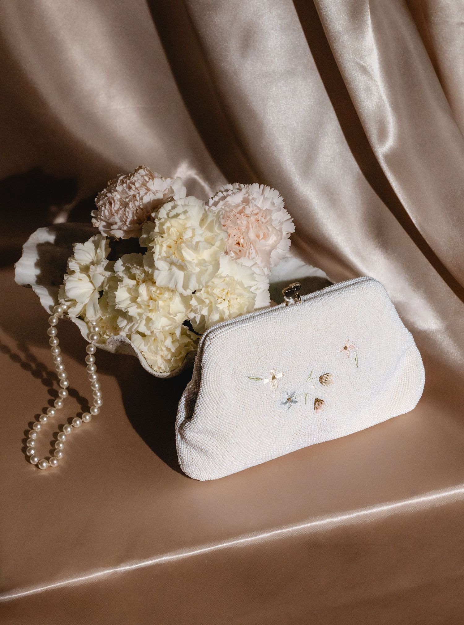 White bridal clutch purse with pearls and floral details on satin background.