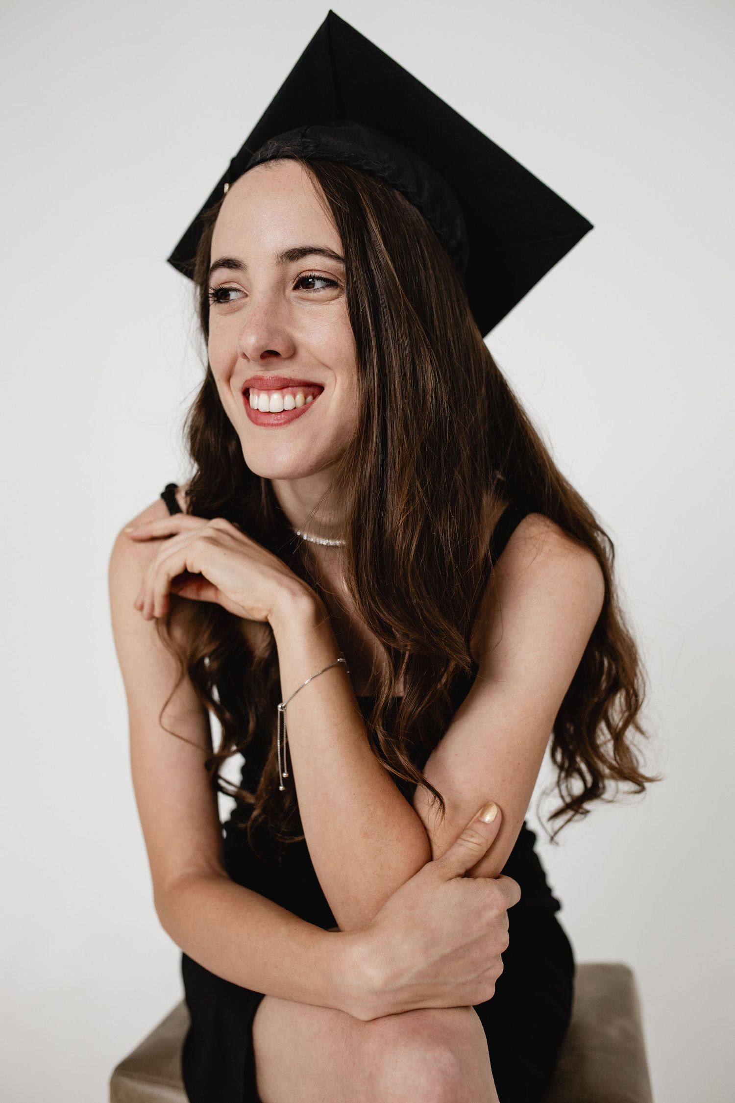 Graduate in black cap and gown smiles joyfully while posing against white background in creative portrait series.