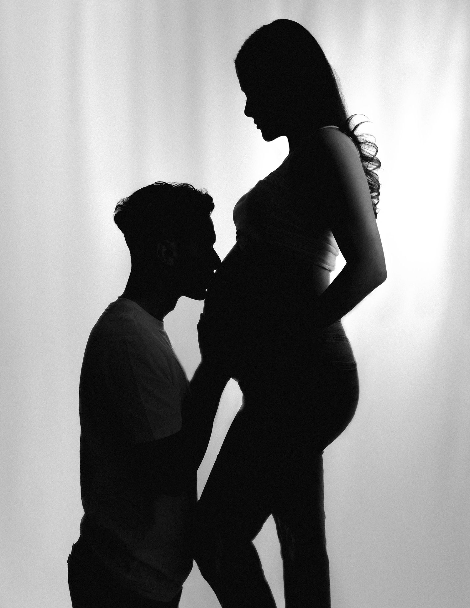 Black and white silhouette of a pregnant woman and partner posing together in a maternity photo shoot.