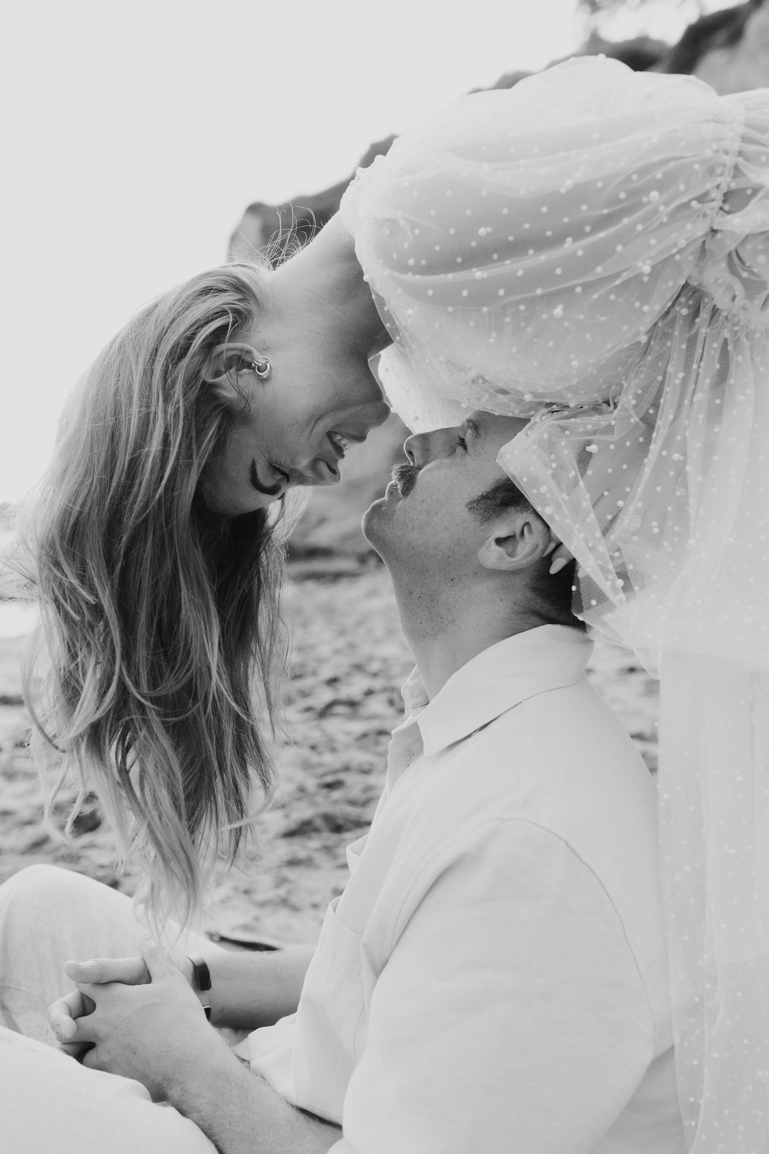 A romantic black and white beach photo sequence showing a couple embracing under a flowing veil.