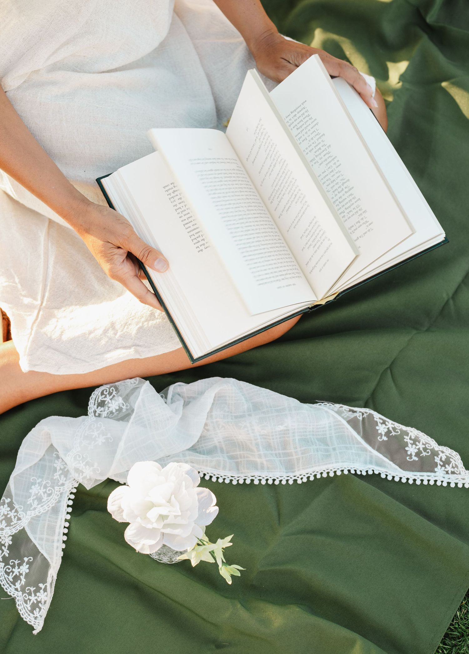Open book on green fabric with delicate lace and white flower details.