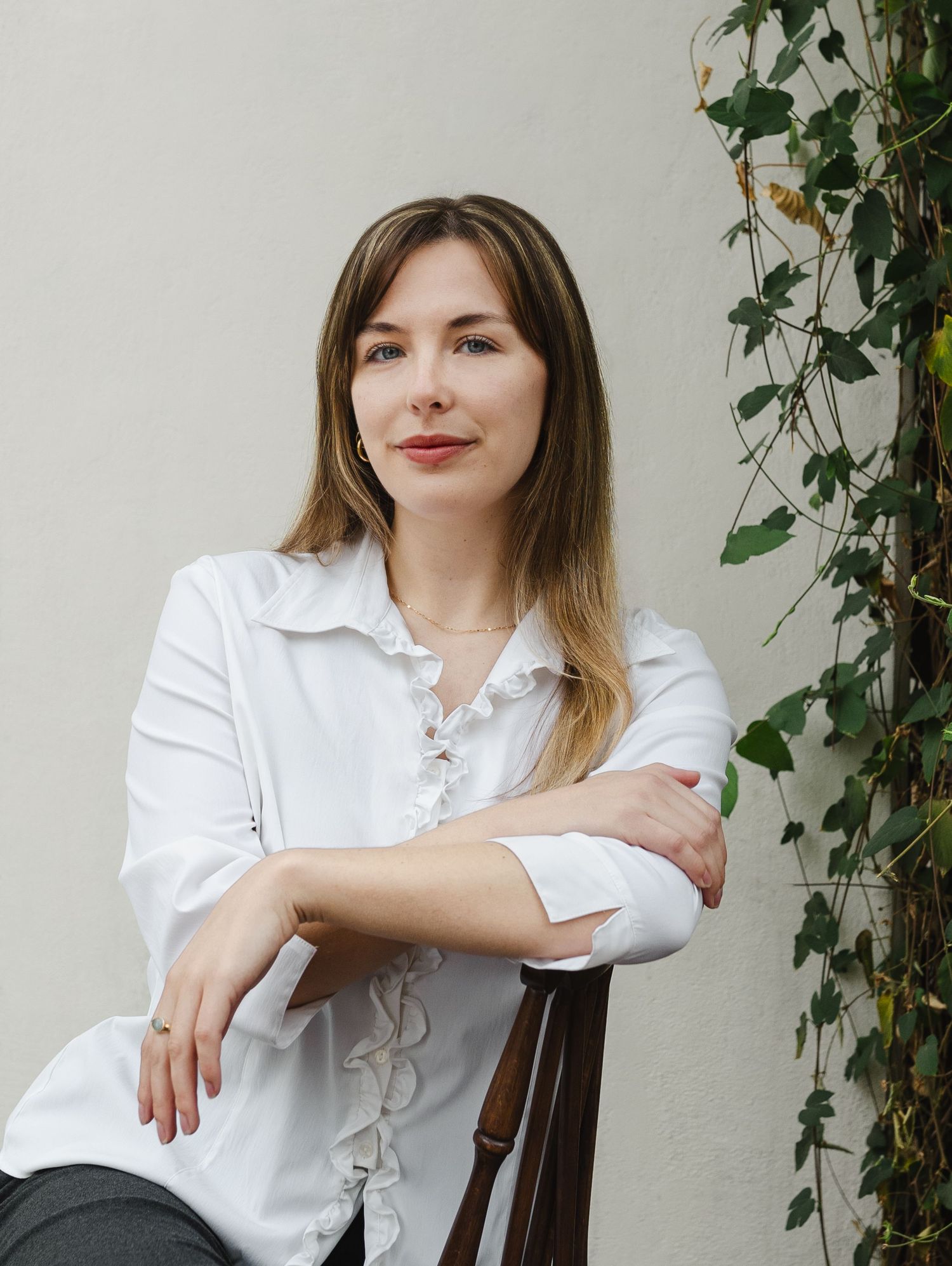 A series of four photos showing someone in a white blouse sitting near green ivy on a light colored wall.