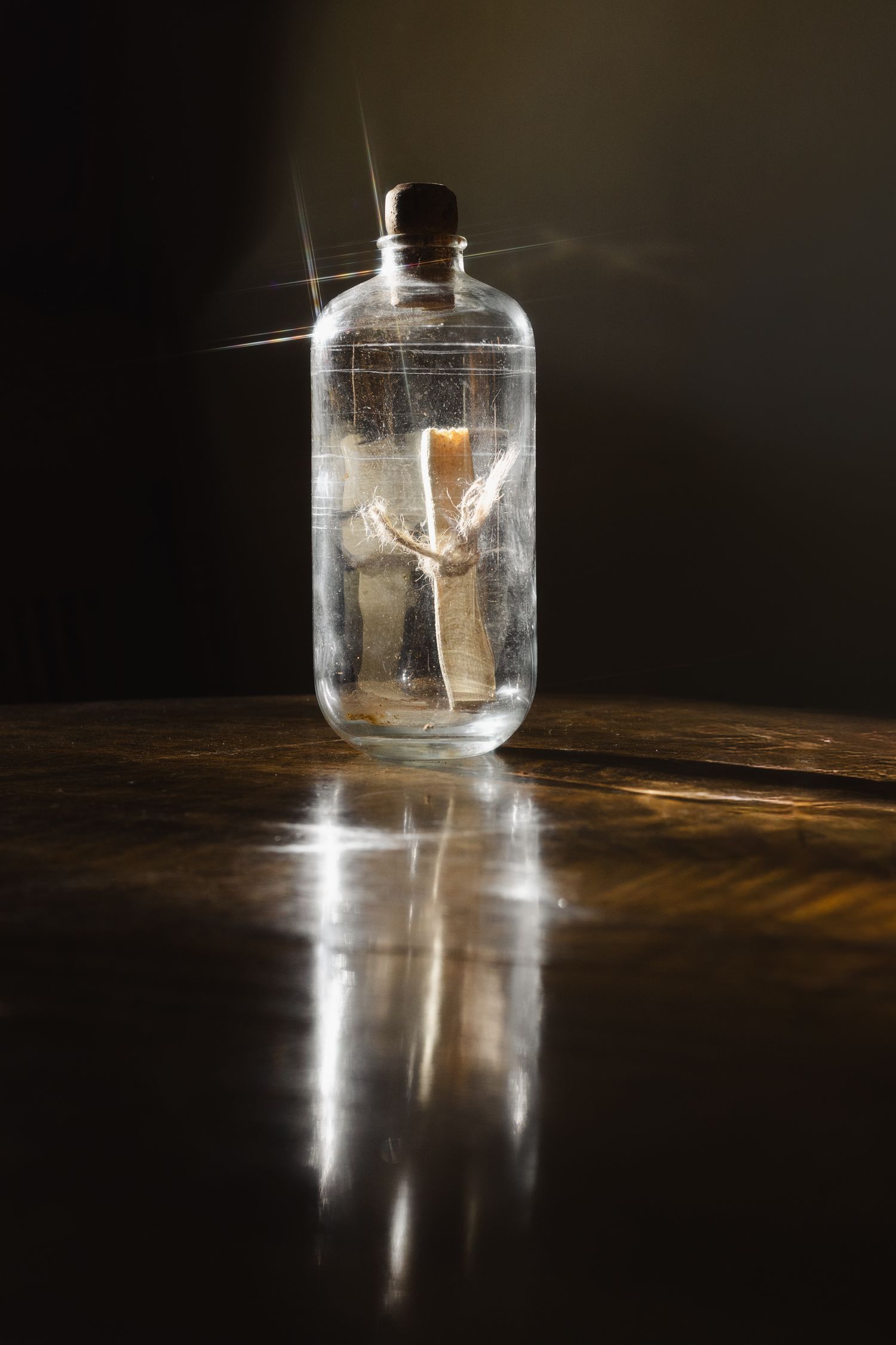 A glass bottle with a cork stopper containing a small figurine, illuminated by dramatic light on a wooden surface.