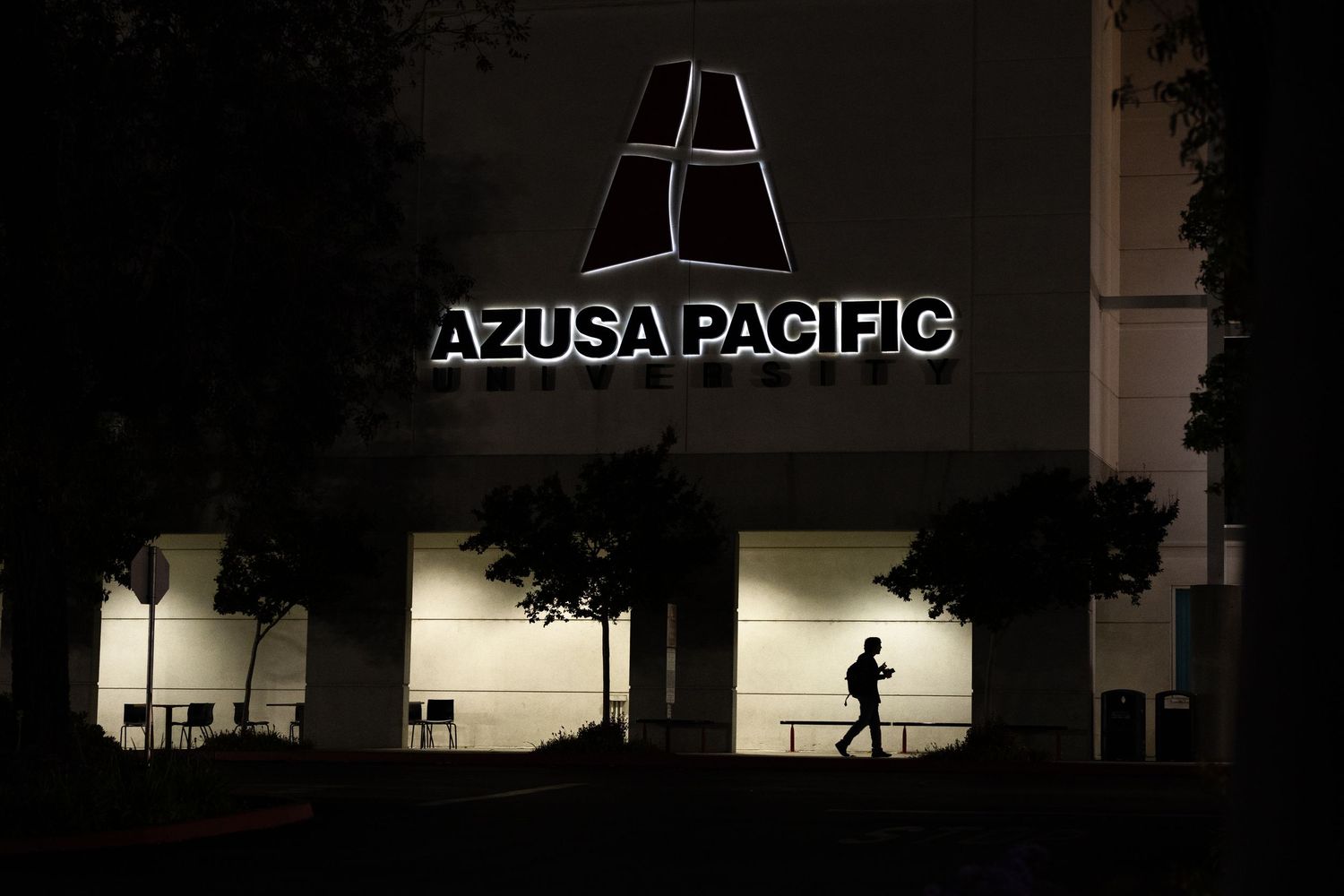 Illuminated Azusa Pacific University sign at night with a silhouetted figure walking beneath.