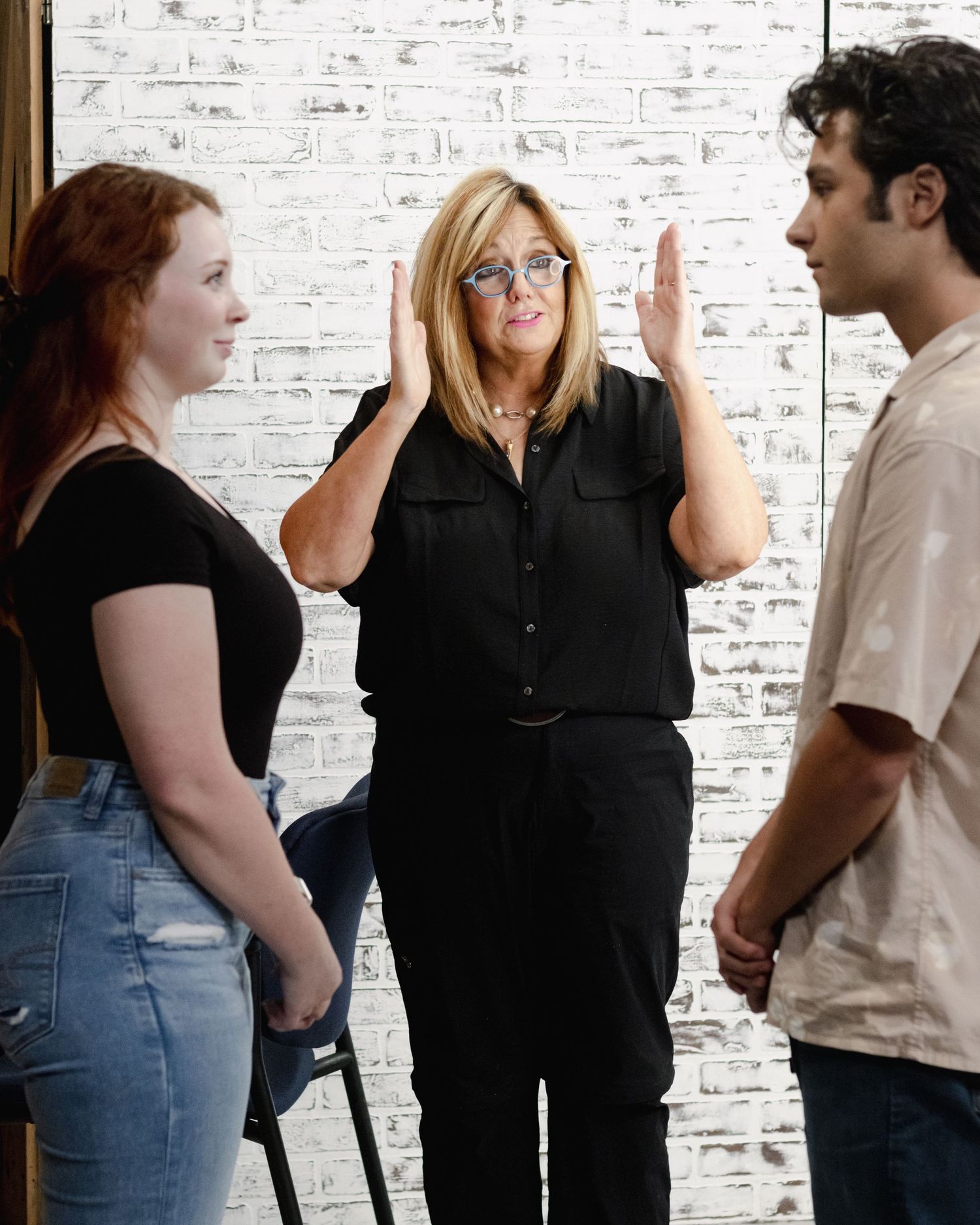 Group of people having a casual conversation against a white brick wall background.