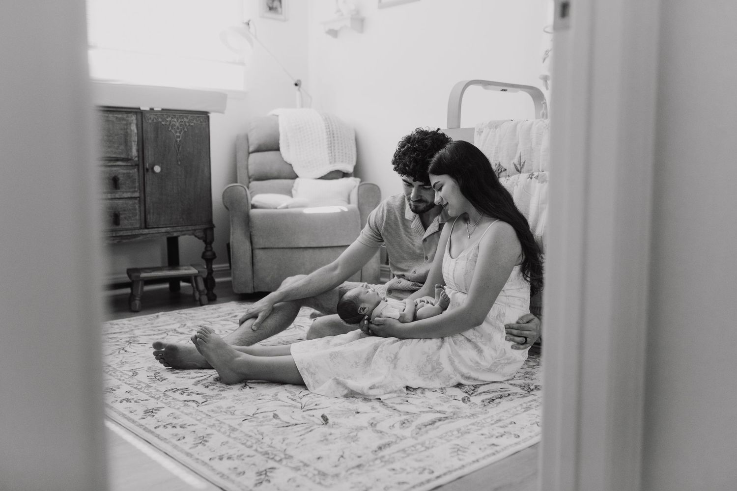 Black and white photo of a couple sitting on a rug on the floor, sharing an intimate moment at home.