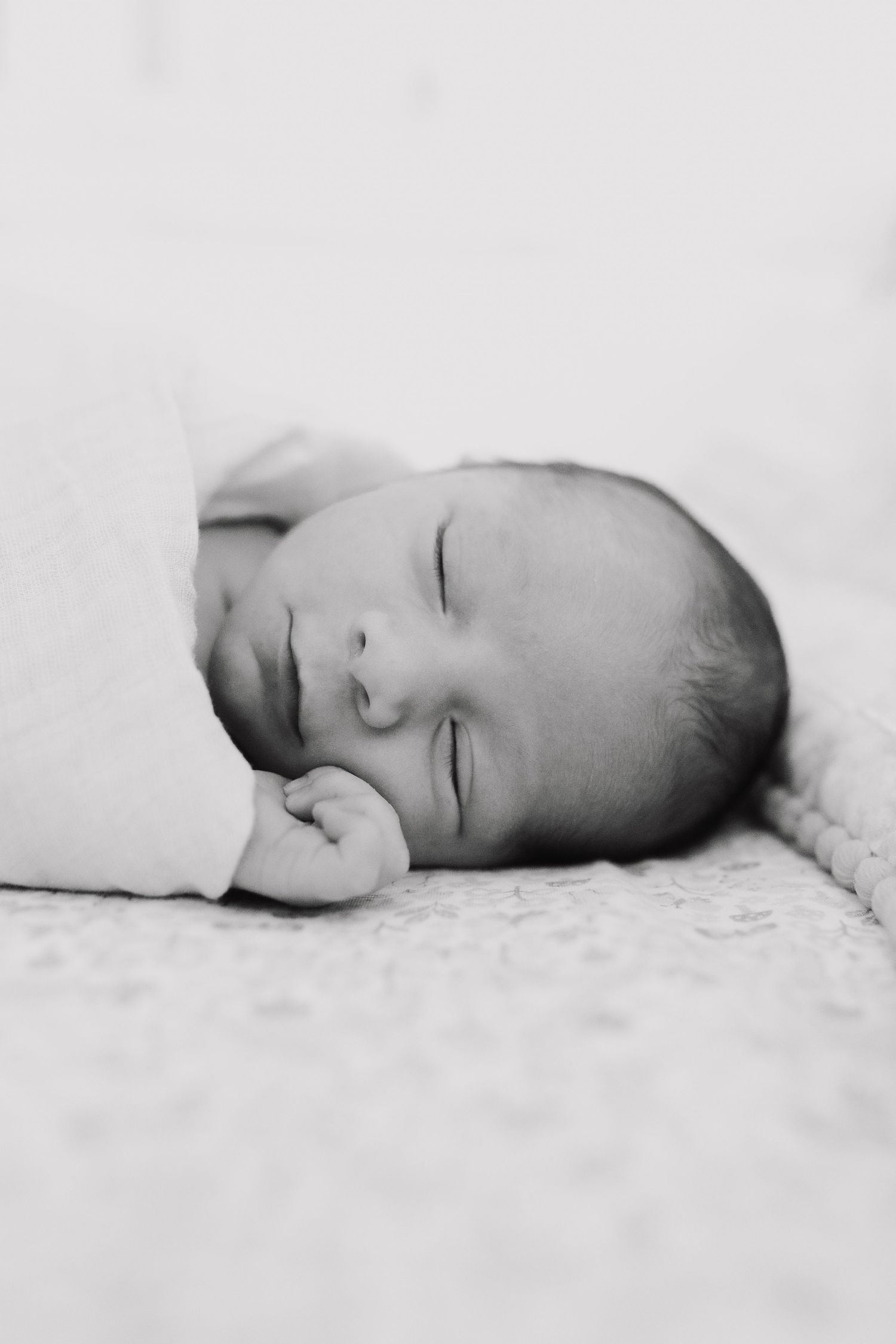 A sleeping newborn baby rests peacefully on soft white bedding in black and white photography.