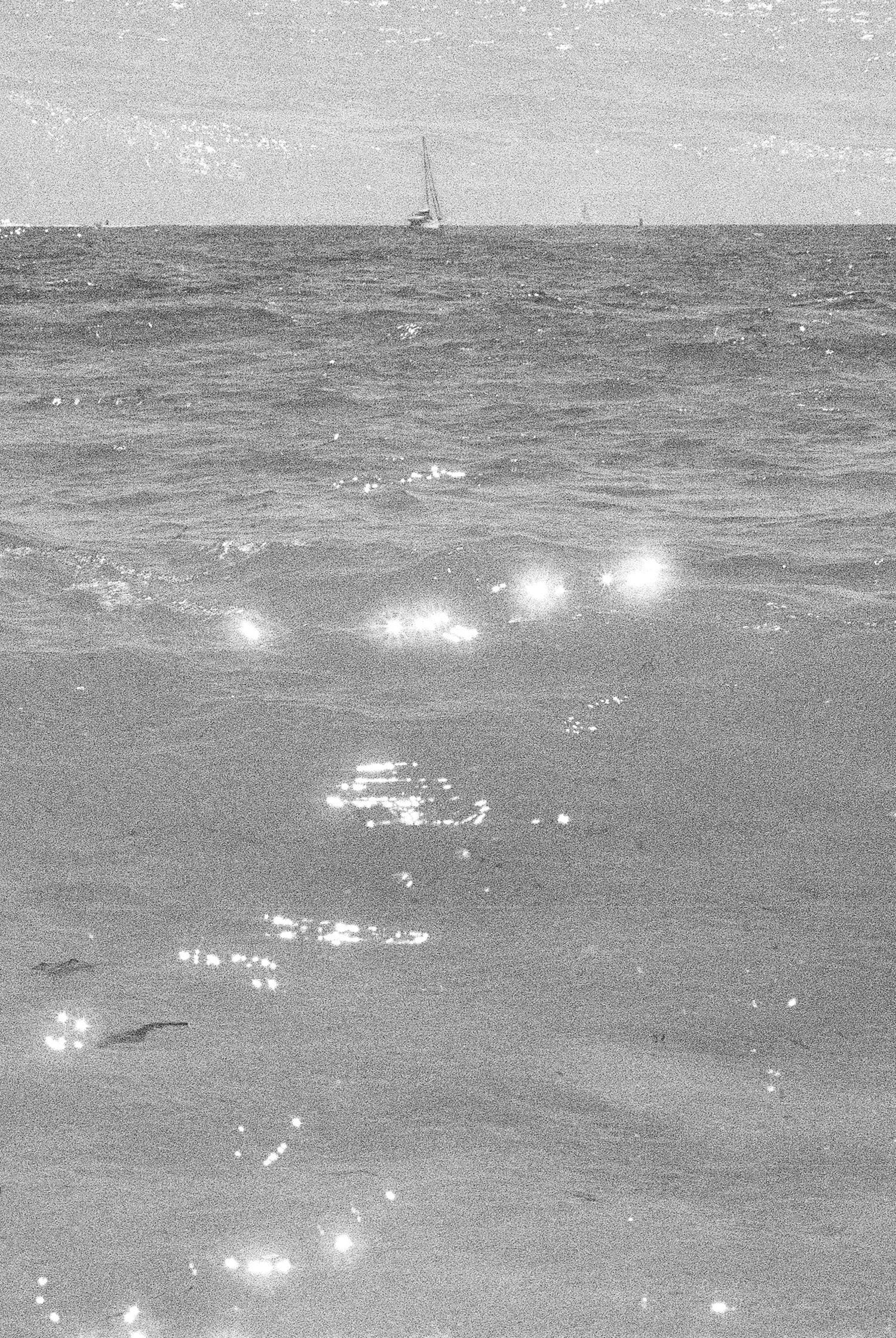 Seascape with sunlight reflecting off rippling ocean waves in black and white.
