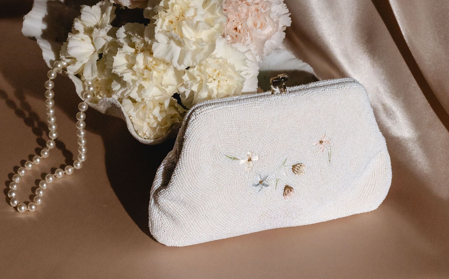 Pearl necklace and white ornamental objects arranged on silk fabric.