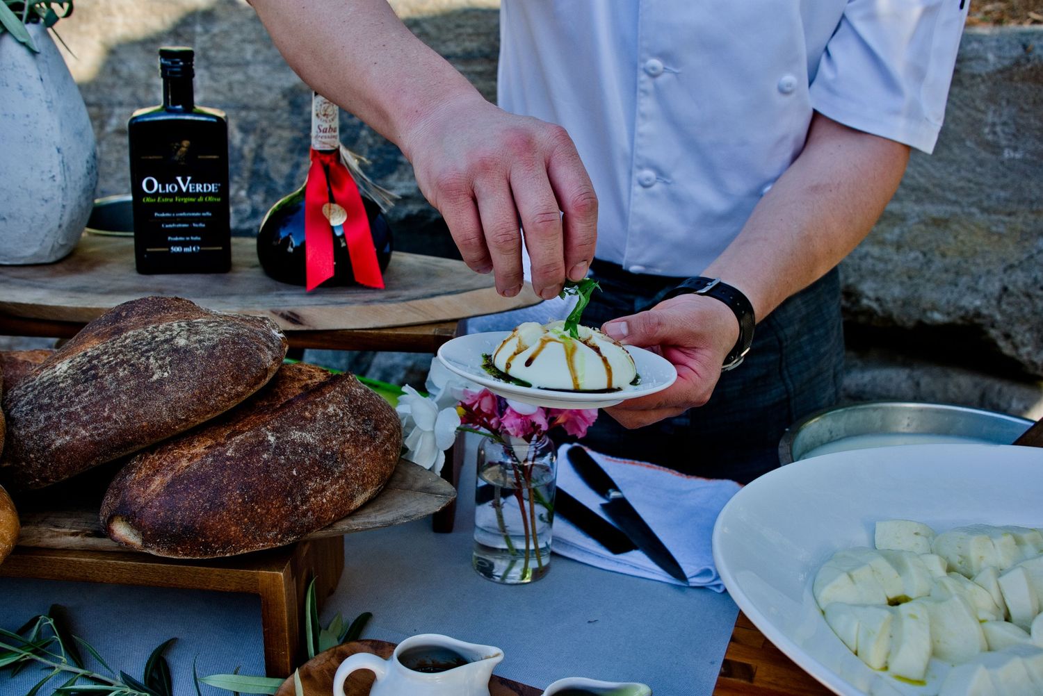 Chef's hands preparing appetizers with artisanal bread and fresh ingredients on rustic wooden board.