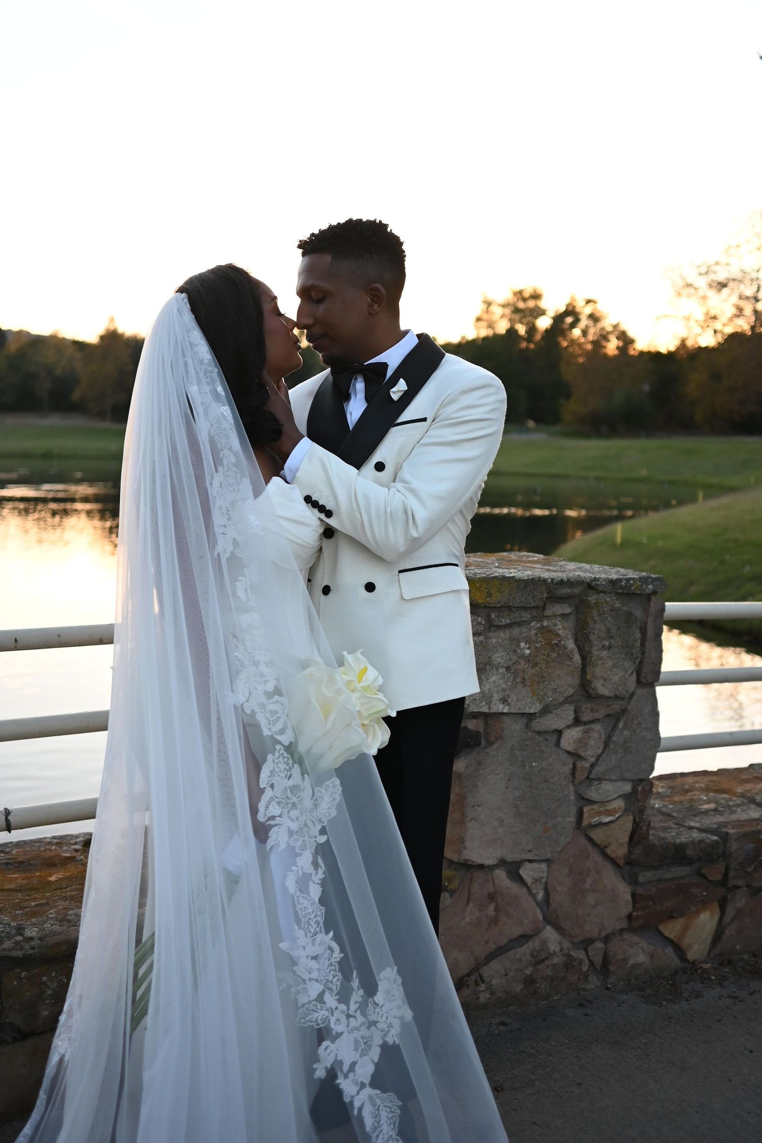 Romantic wedding couple shares intimate moments at sunset by a stone wall and lake in a series of silhouetted photos.