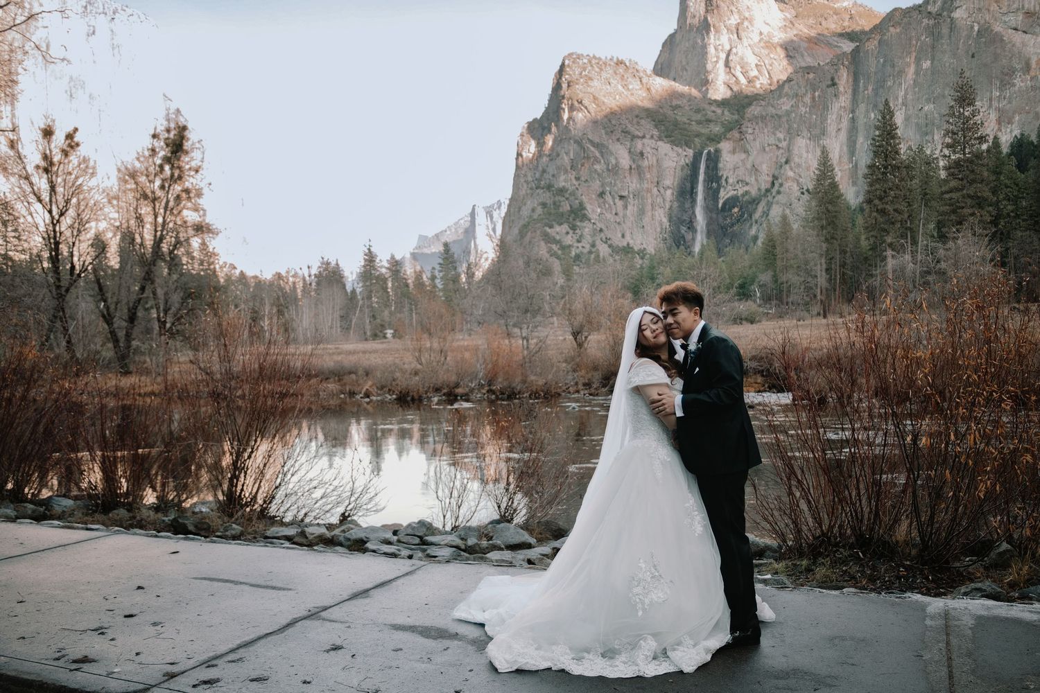 A couple in wedding attire embraces against the dramatic backdrop of Yosemite Valley's towering granite cliffs.