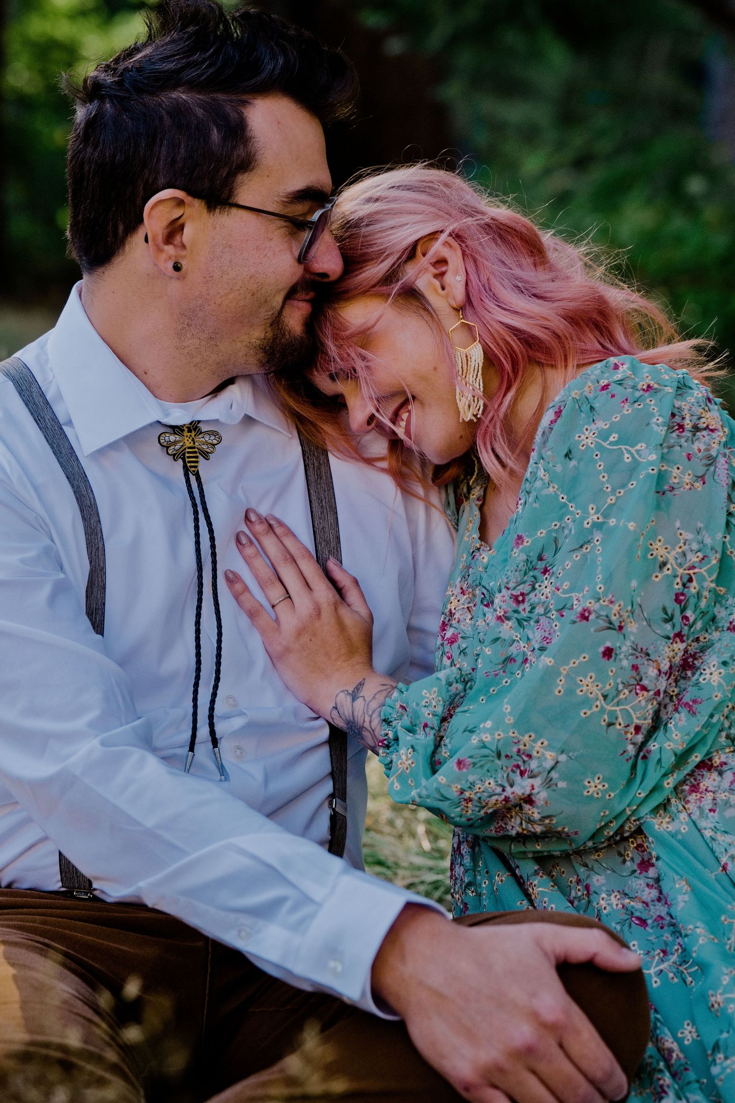 A romantic outdoor portrait shows a couple in vintage-inspired attire sharing an intimate moment among green foliage.