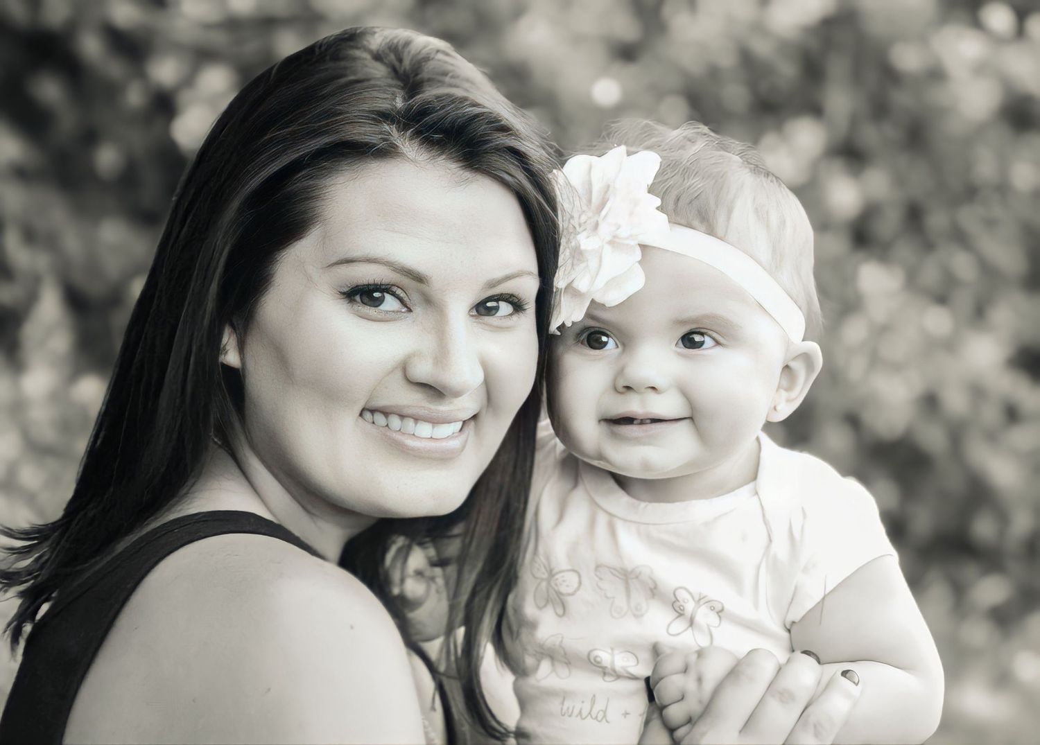 Black and white portrait of a parent and baby wearing a white headband set against a soft blurred background.