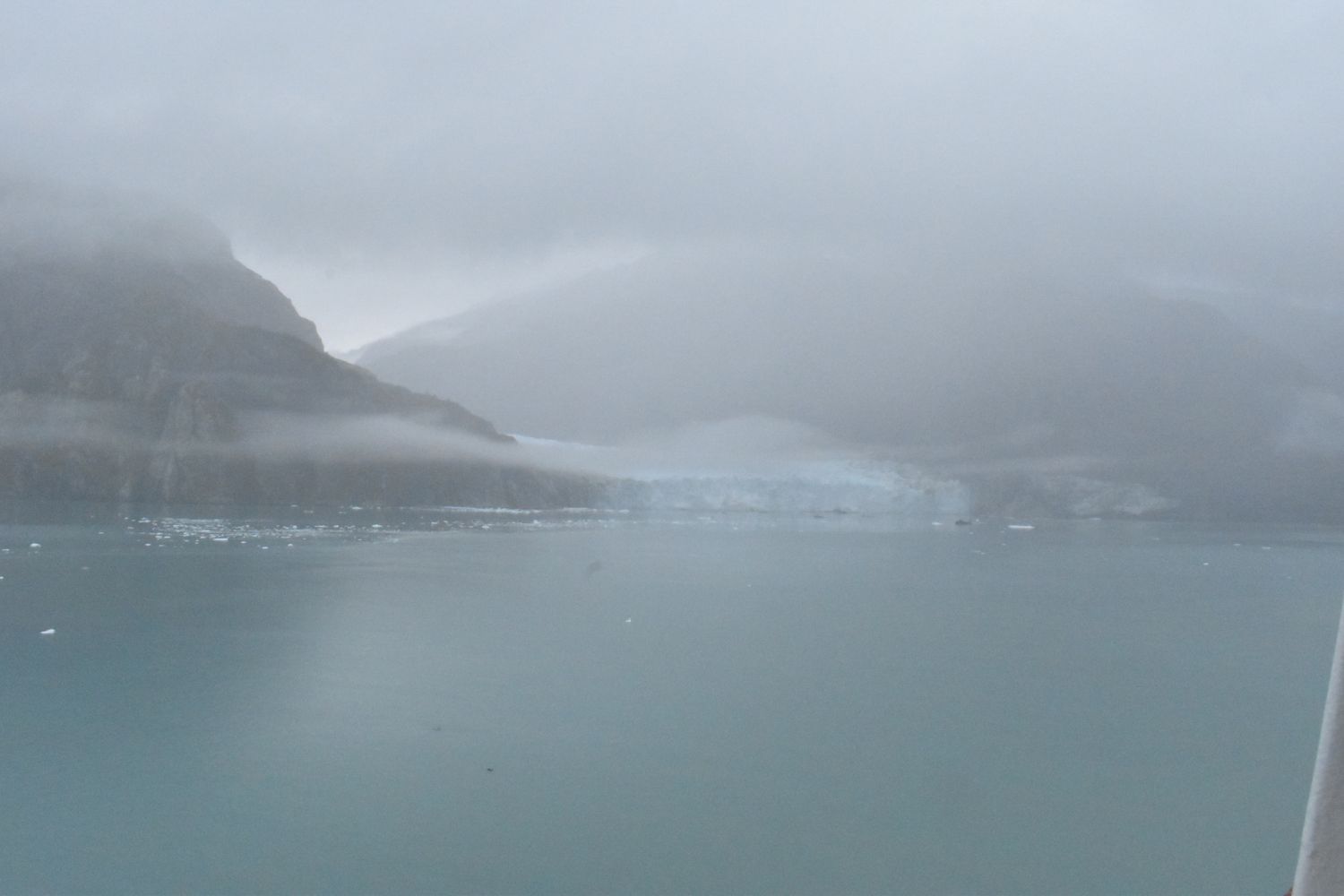 A series of misty fjords in Norway with dramatic mountain peaks rising from calm waters in foggy conditions.