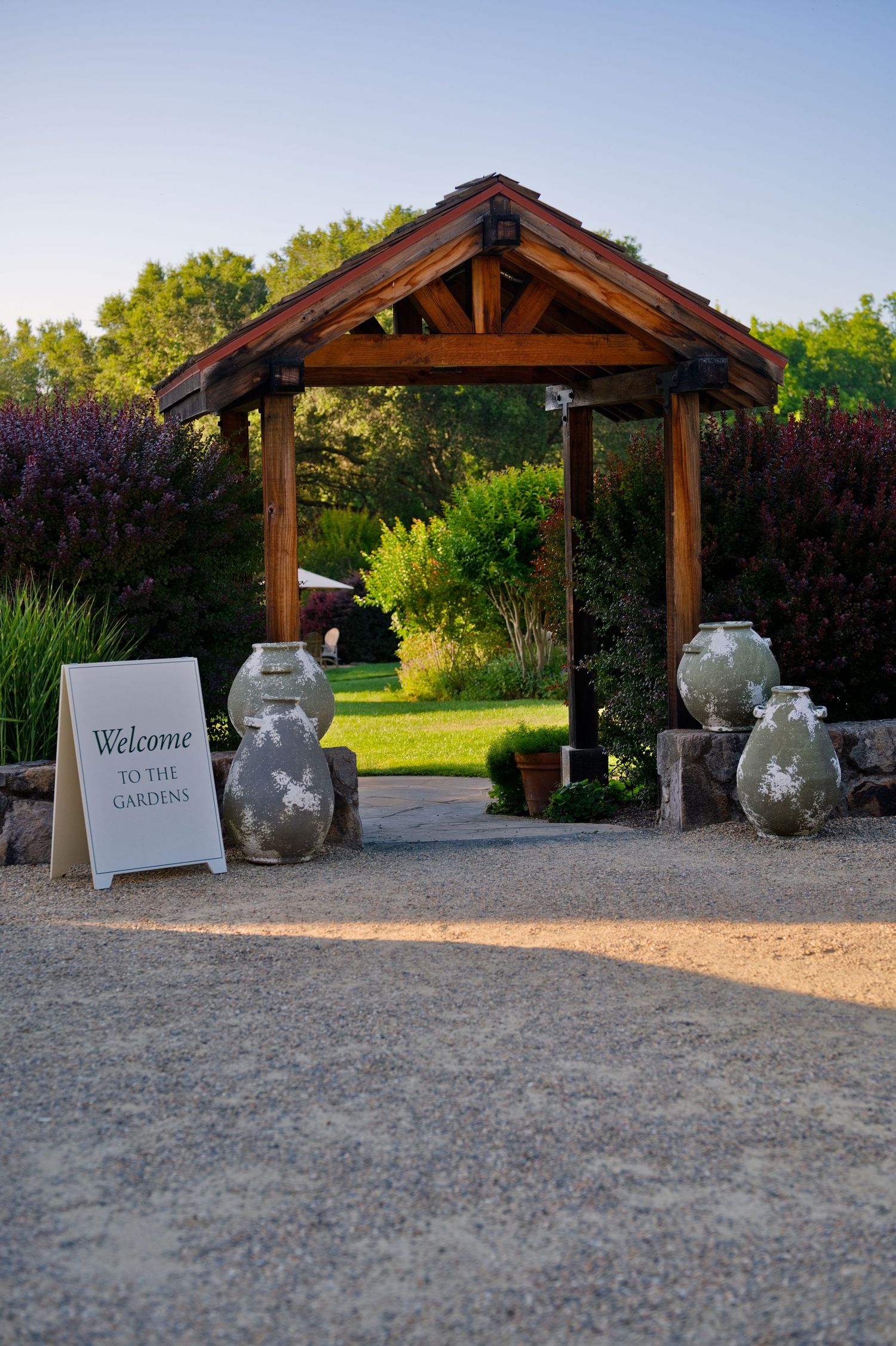 Rustic wooden gazebo entrance with decorative mason jars and welcome sign along a gravel pathway at an outdoor venue.