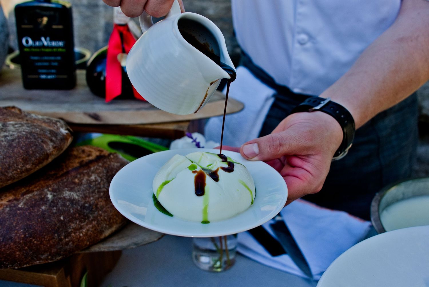Chef pours dark sauce onto a white dessert plate in an artistic plating presentation.