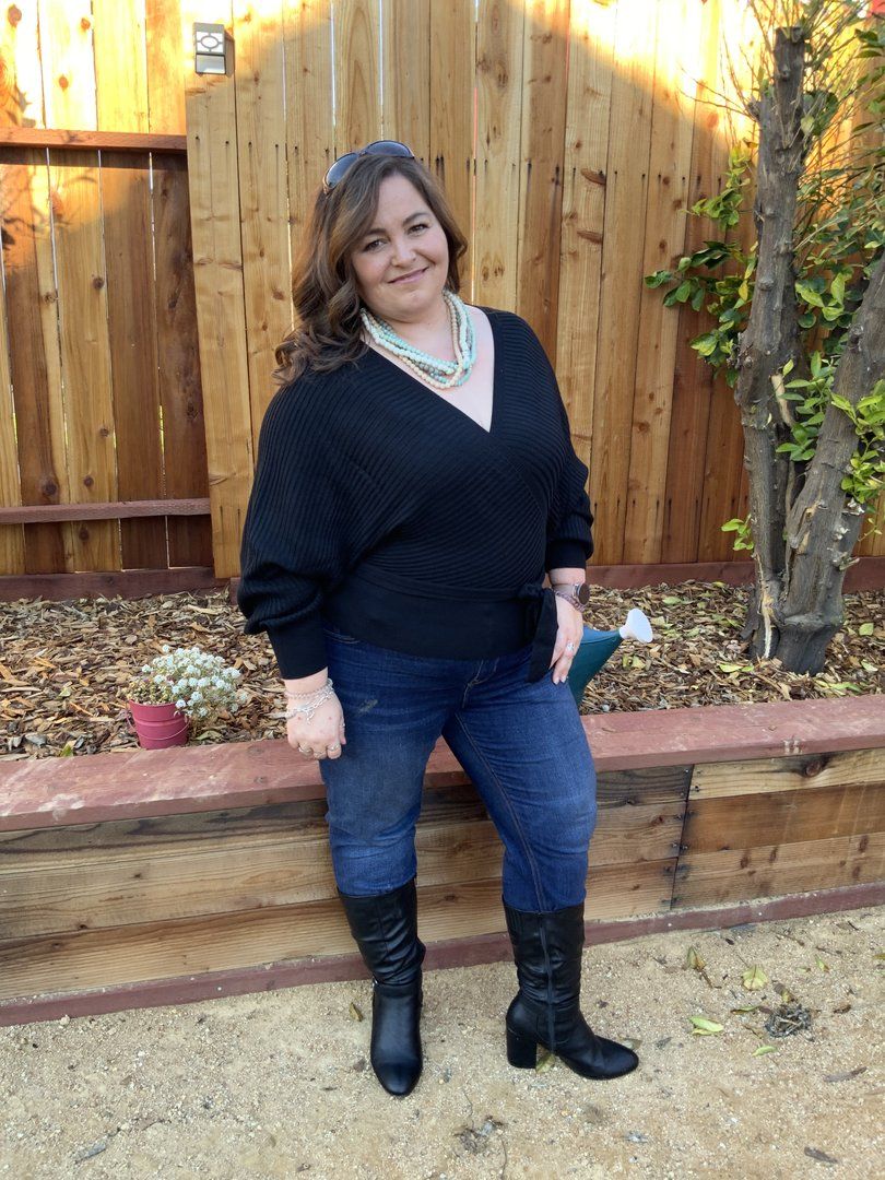 Person in a black top sitting outside on a wooden deck surrounded by a natural fence in warm lighting.