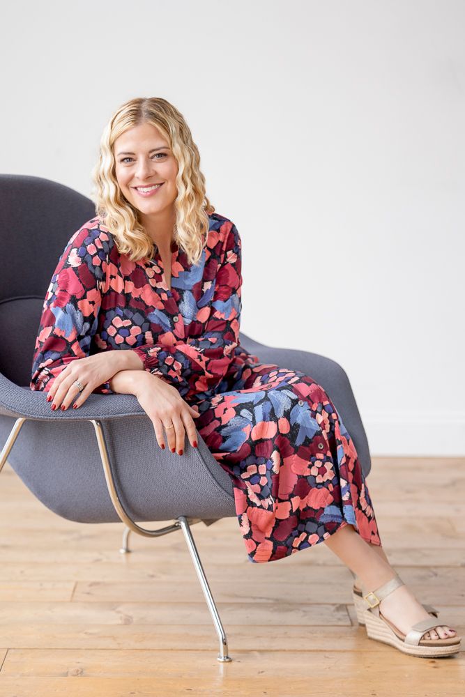 A person in a floral print dress relaxes in different poses on a modern gray lounge chair against a white backdrop.