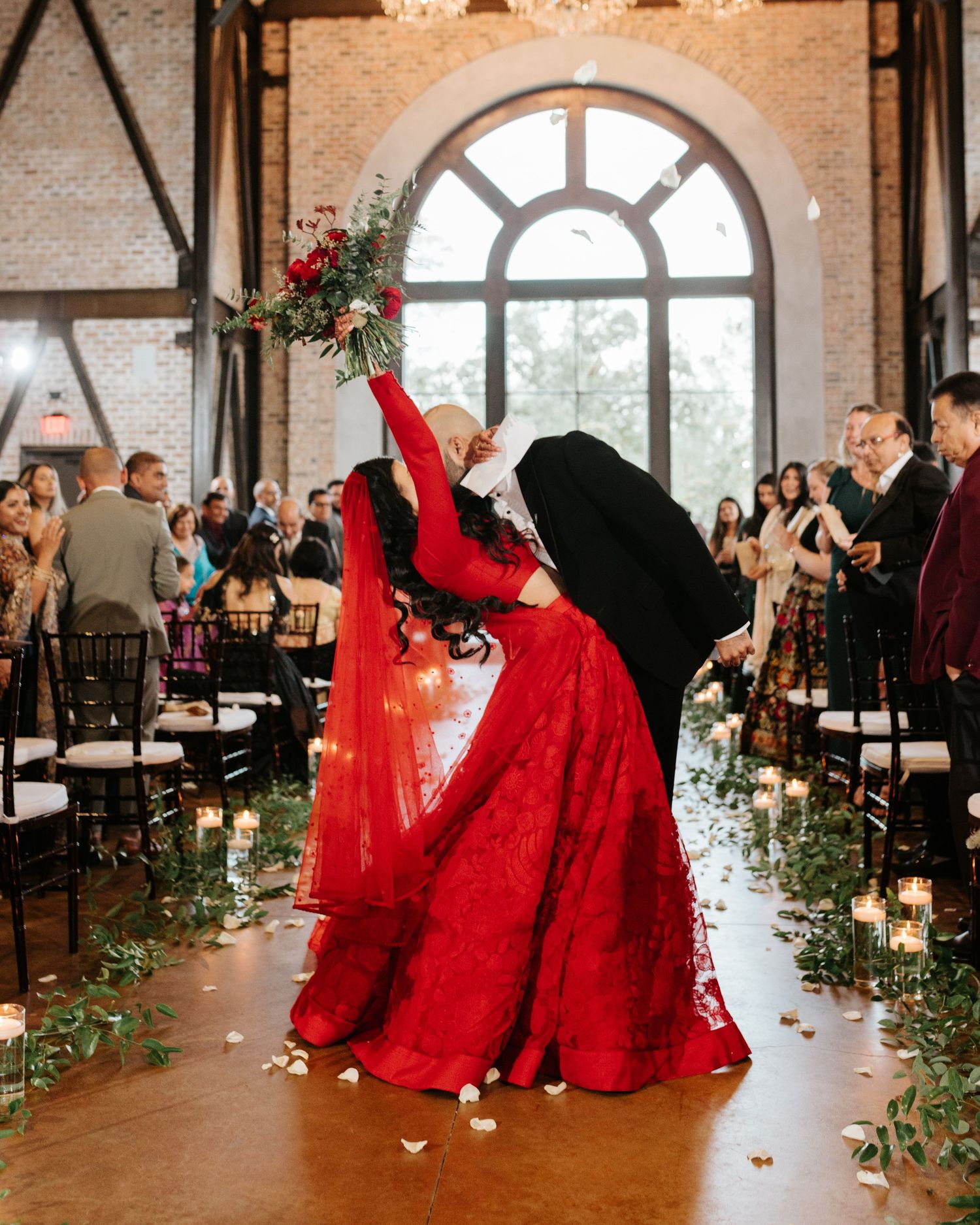 Couple dancing in rustic venue with red dress twirling dramatically among floral decor.