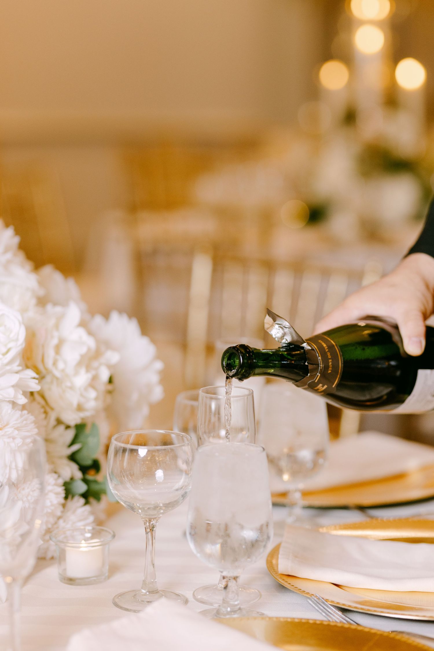 Wine being poured into glass at elegant wedding reception table with white floral centerpieces.