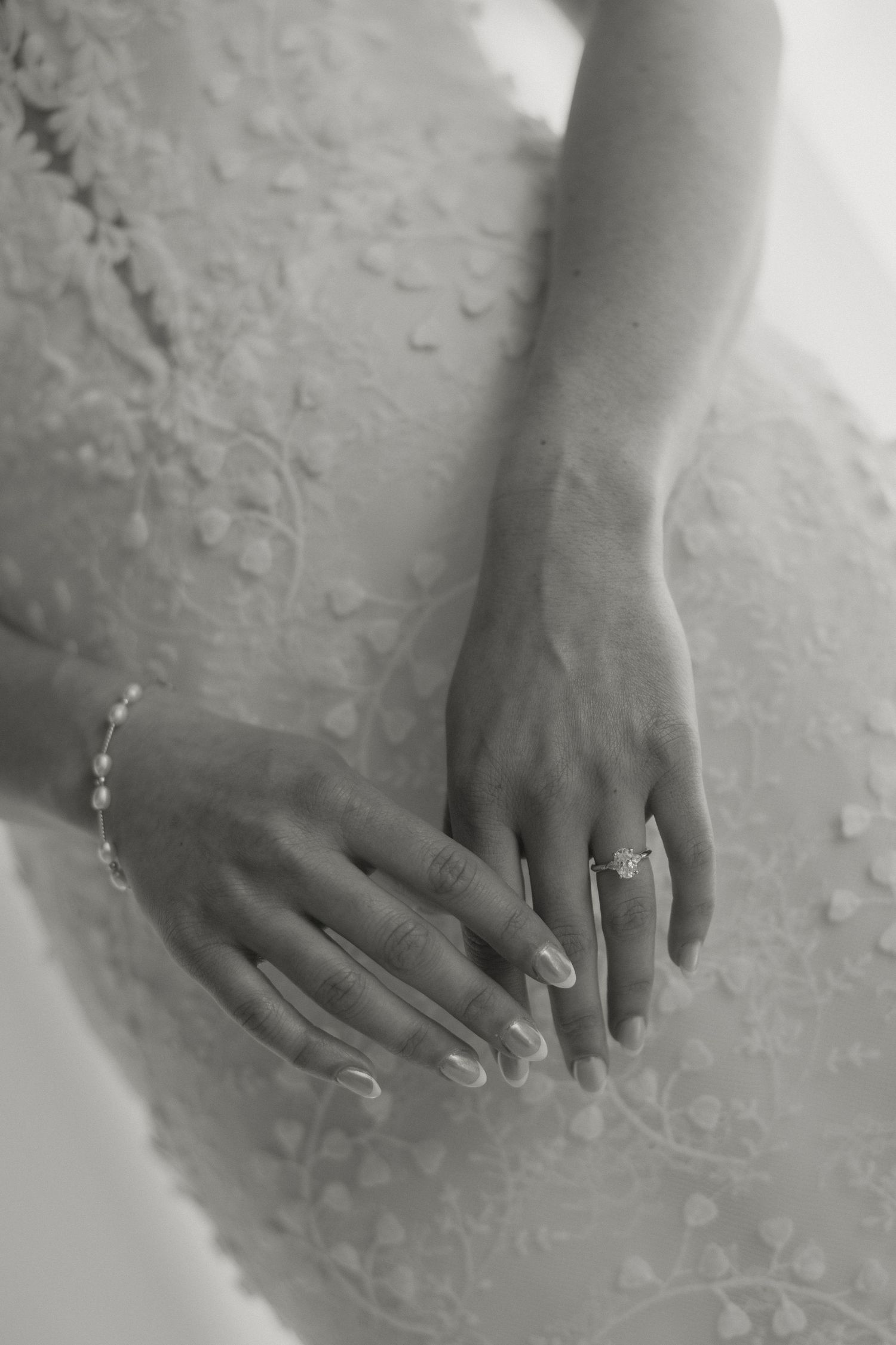 Black and white close-up photo of hands wearing engagement rings against a textured white background.