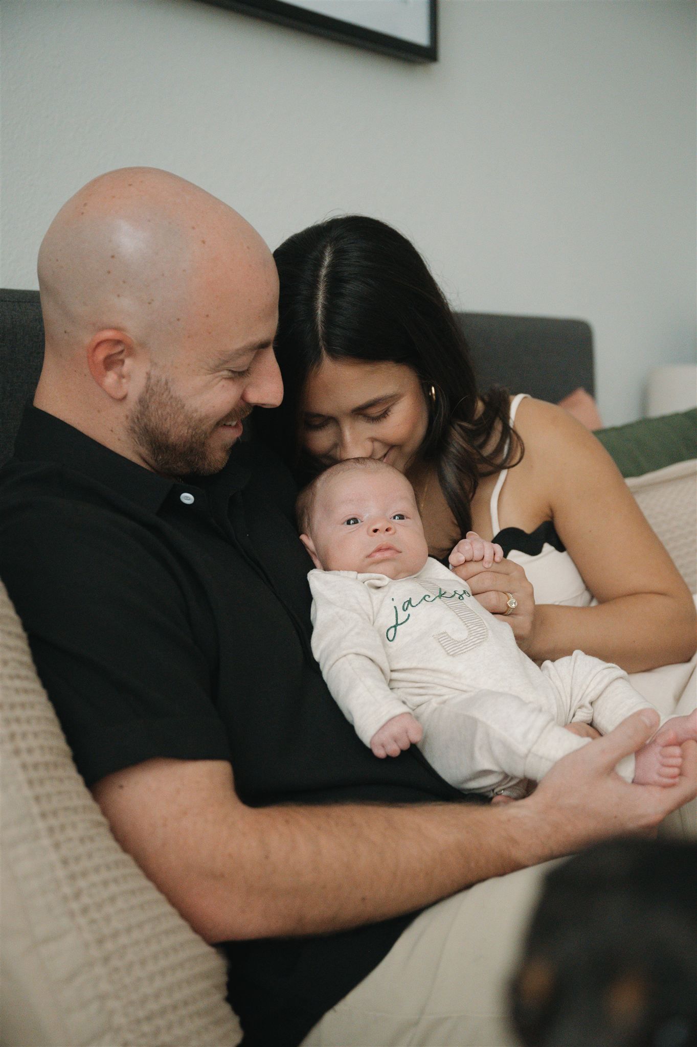 Family shares tender moment with newborn baby while snuggled up on the bed together.