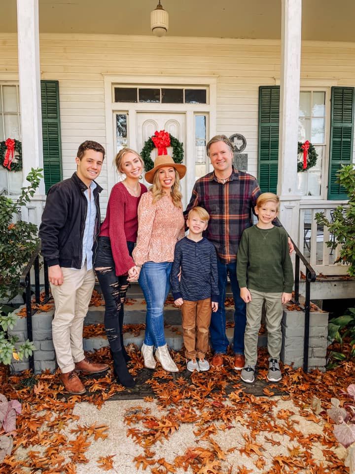 A group stands together on a porch with autumn leaves scattered around them during a fall family photo session.