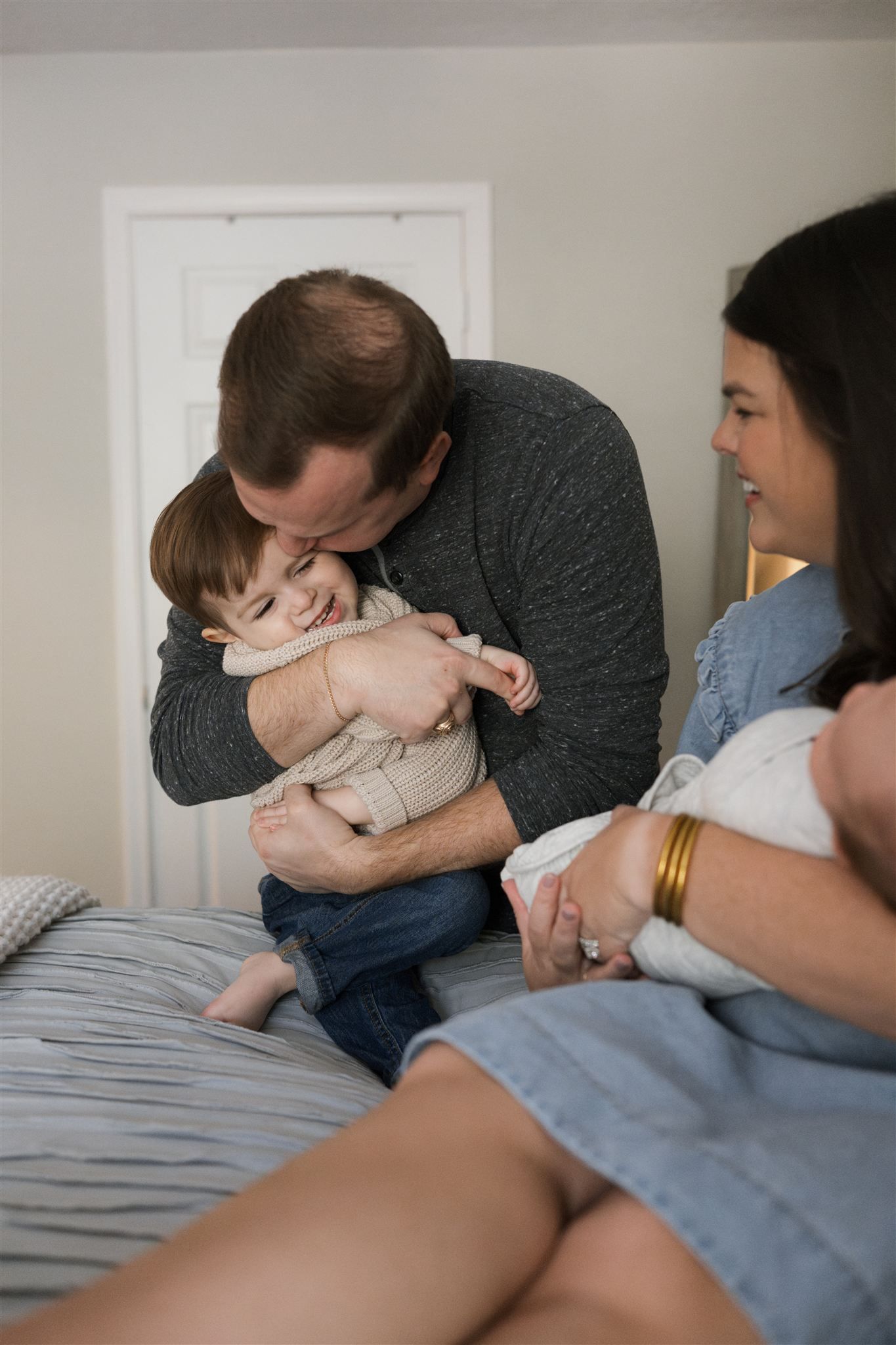 A sequence of tender moments showing a parent cradling and comforting a small baby on a bed with gray bedding.