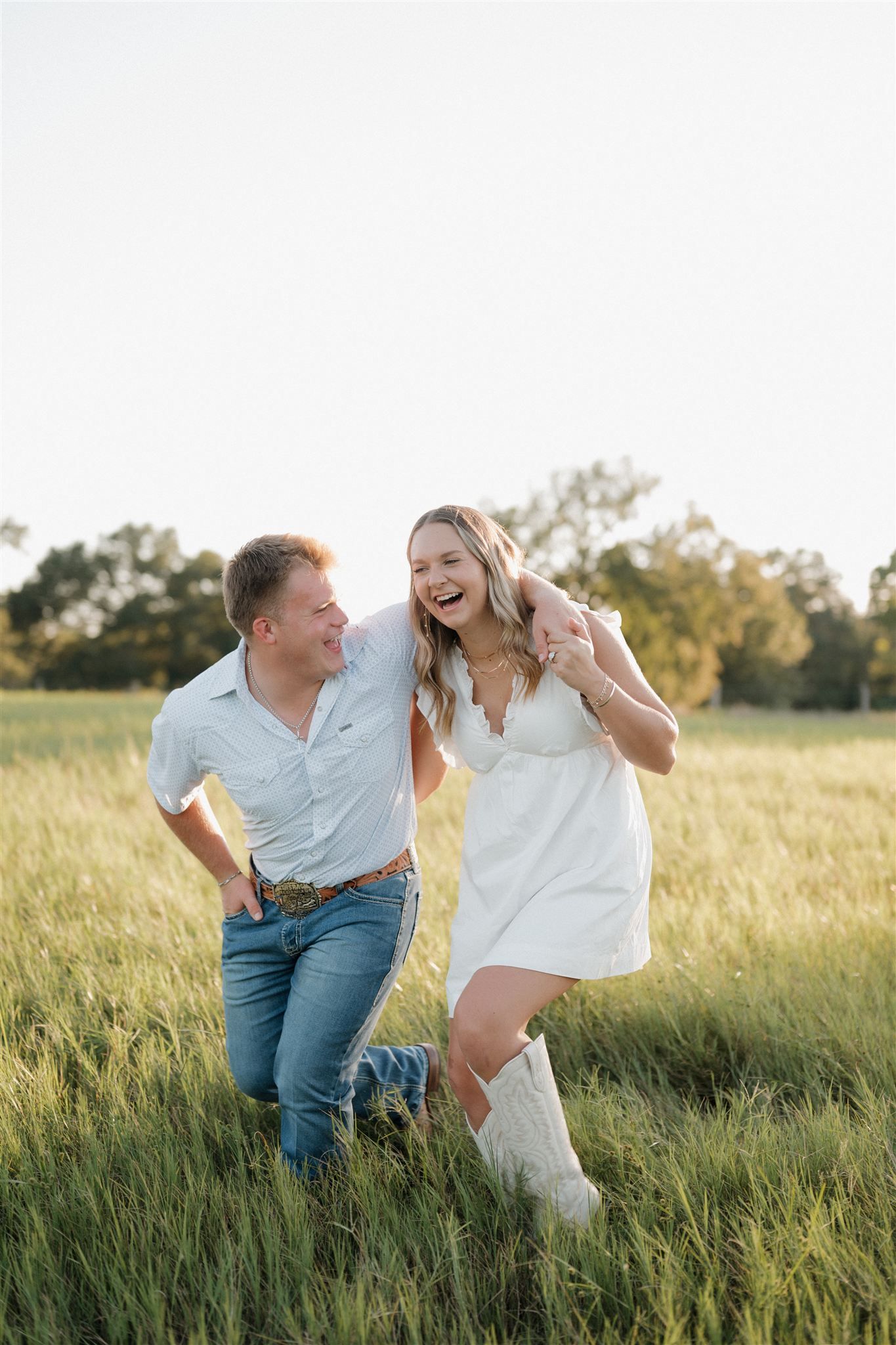 A couple dances and laughs together in a golden wheat field during sunset.