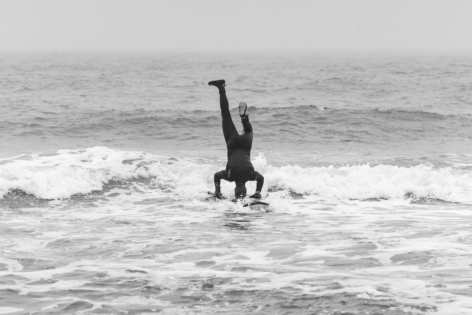 A portrait photo of a man doing a headstand on his surfboard in the ocean