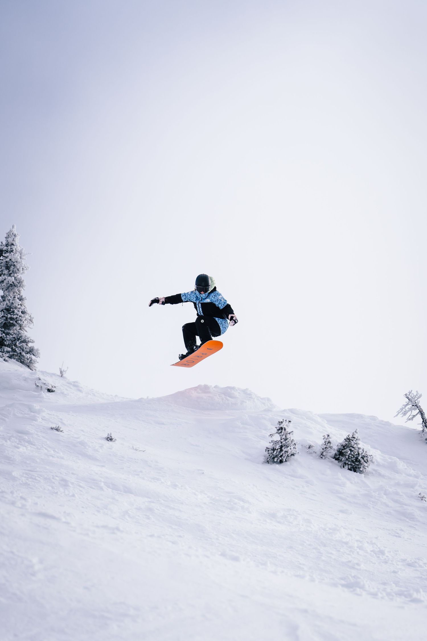 Snowboarder performs aerial jump against white winter mountain landscape.